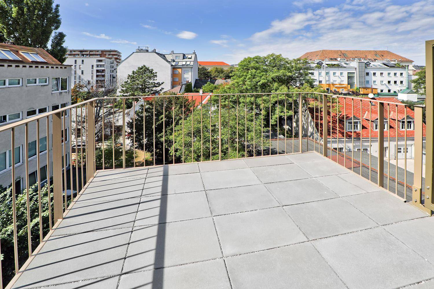 Helle Dachterrasse mit Fliesenboden und Blick auf die umliegenden Wohngebäude und Grünflächen.