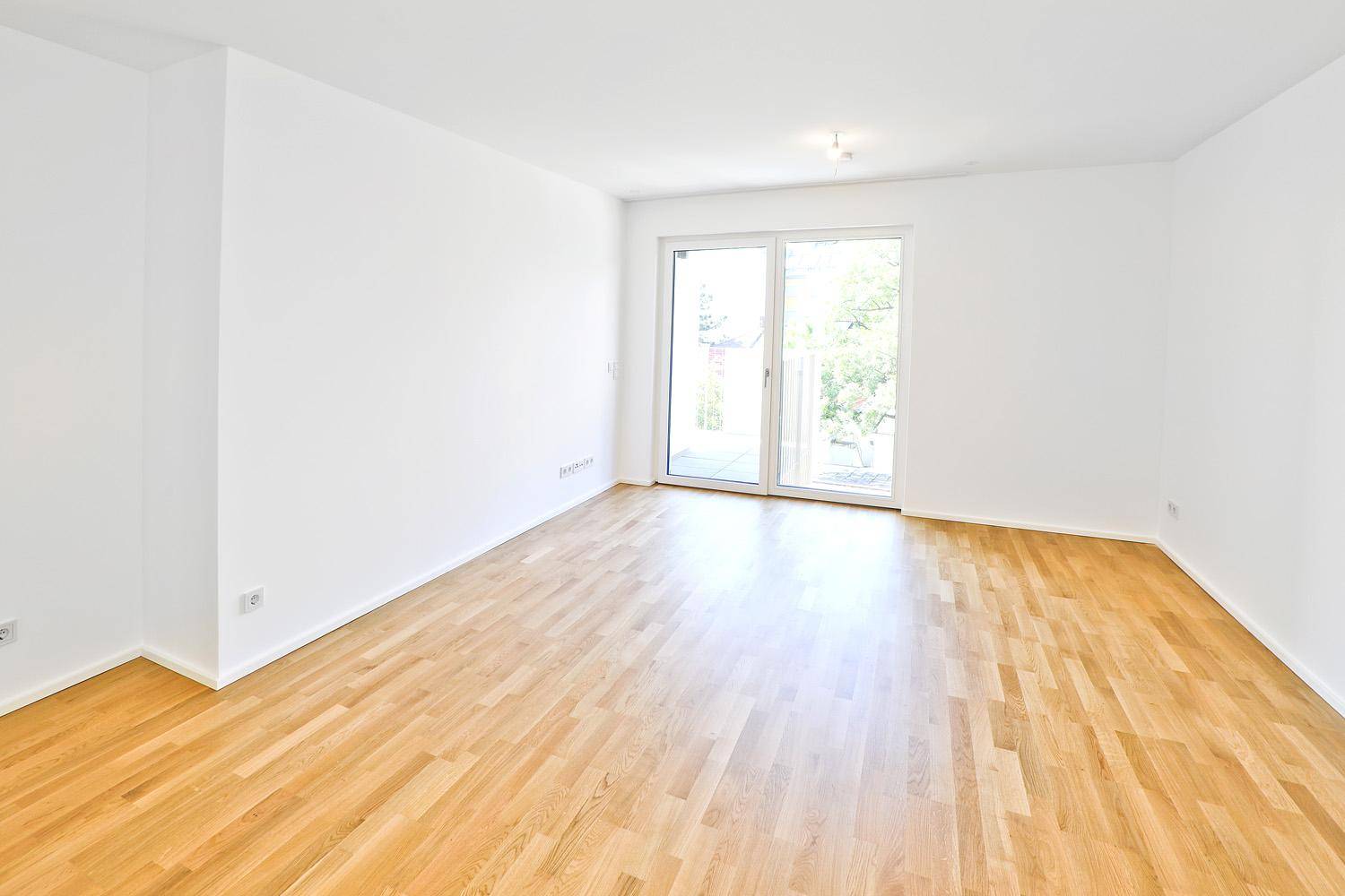 Helles, leeres Zimmer mit Parkettboden und Zugang zu einem Balkon.