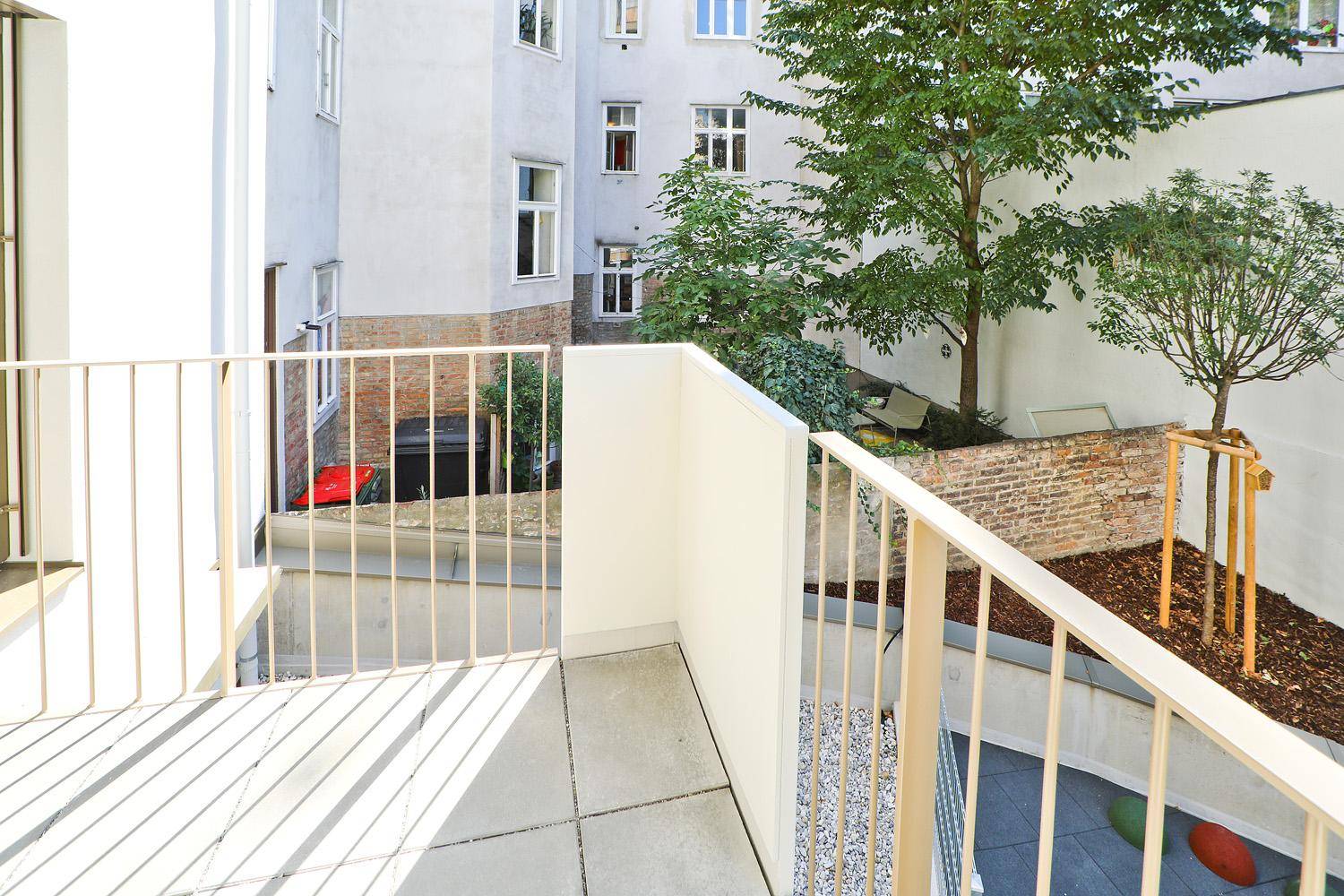 Sonnige Terrasse mit hellem Boden und Blick auf den ruhigen Innenhof und die Fassade.