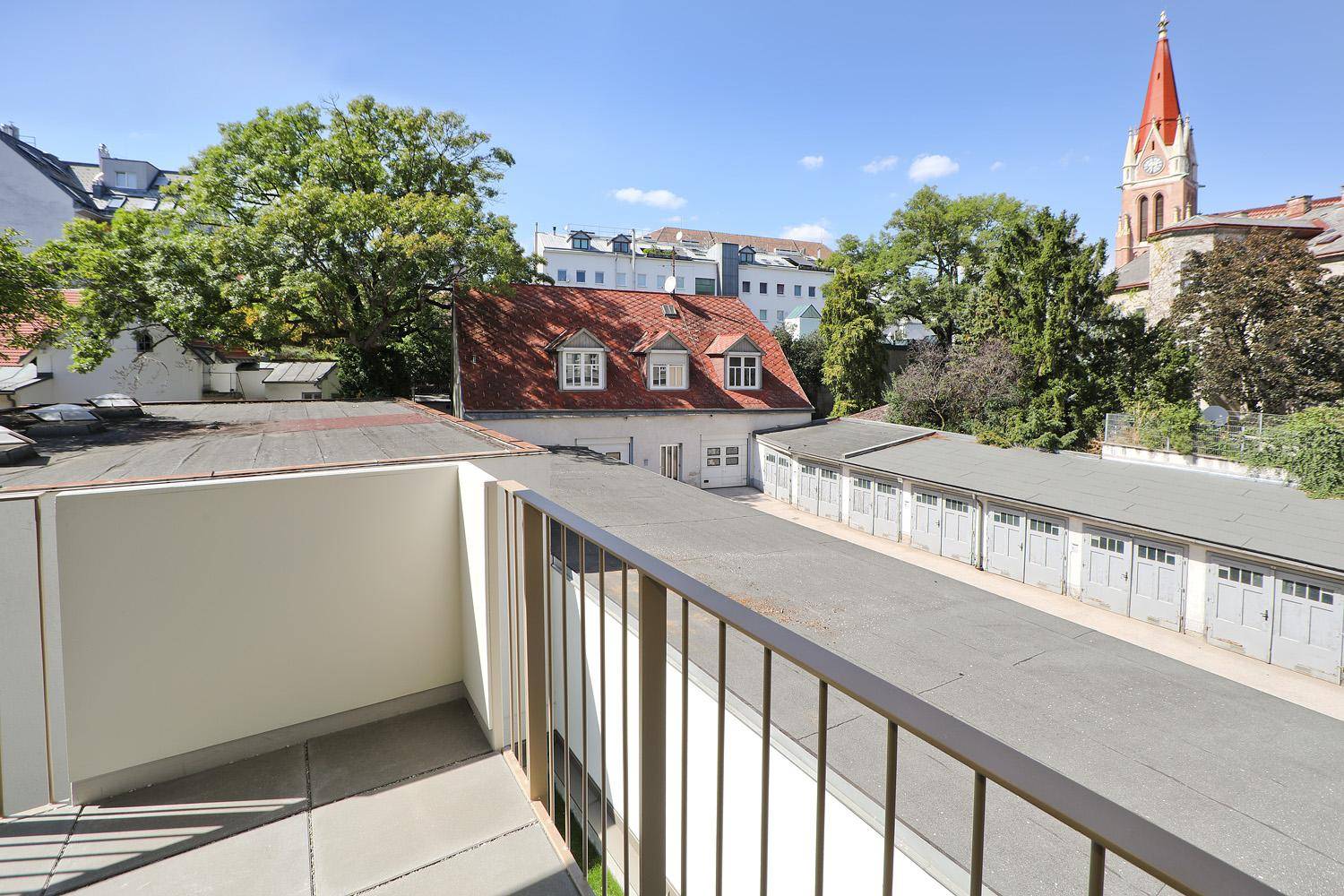 Sonniger Balkon mit Blick auf die Nachbarschaft und einen Kirchturm.