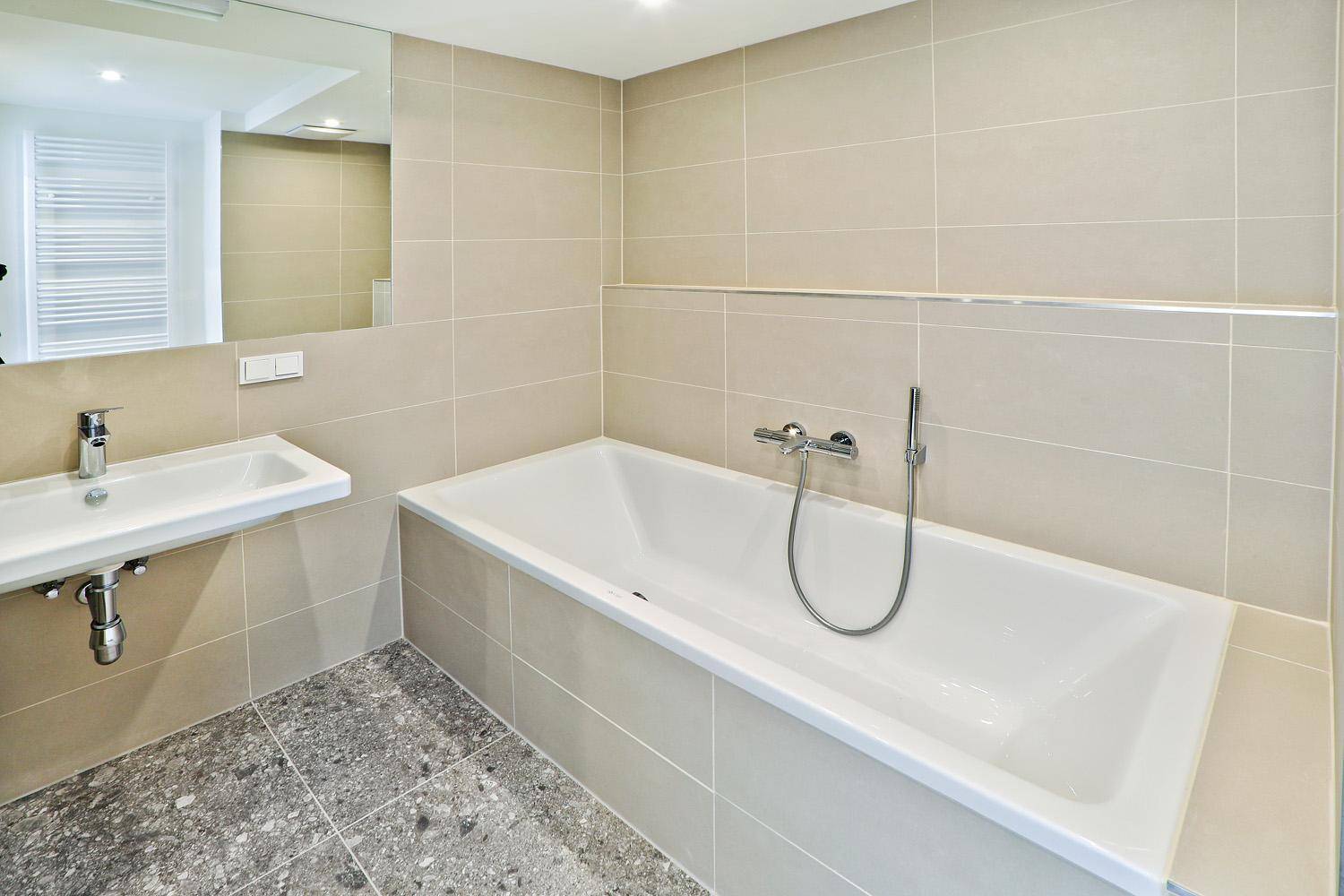 Modernes Badezimmer mit Badewanne, Einzelwaschbecken und großen Fliesen.