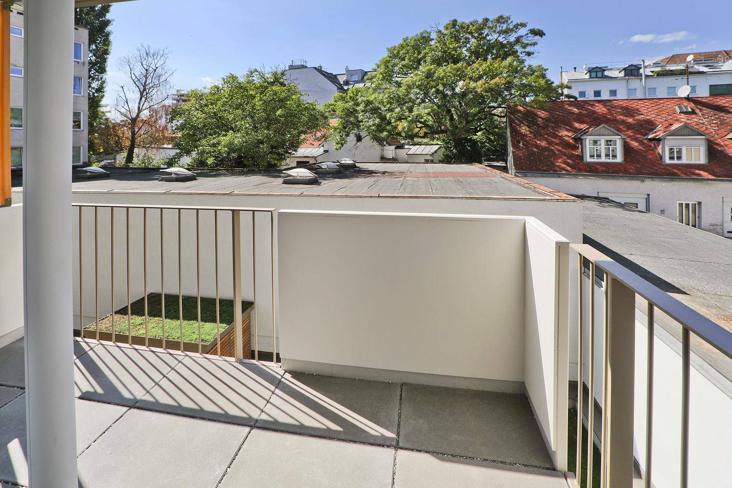 Heller Balkon mit Fliesenboden und einem kleinen Grünbereich.