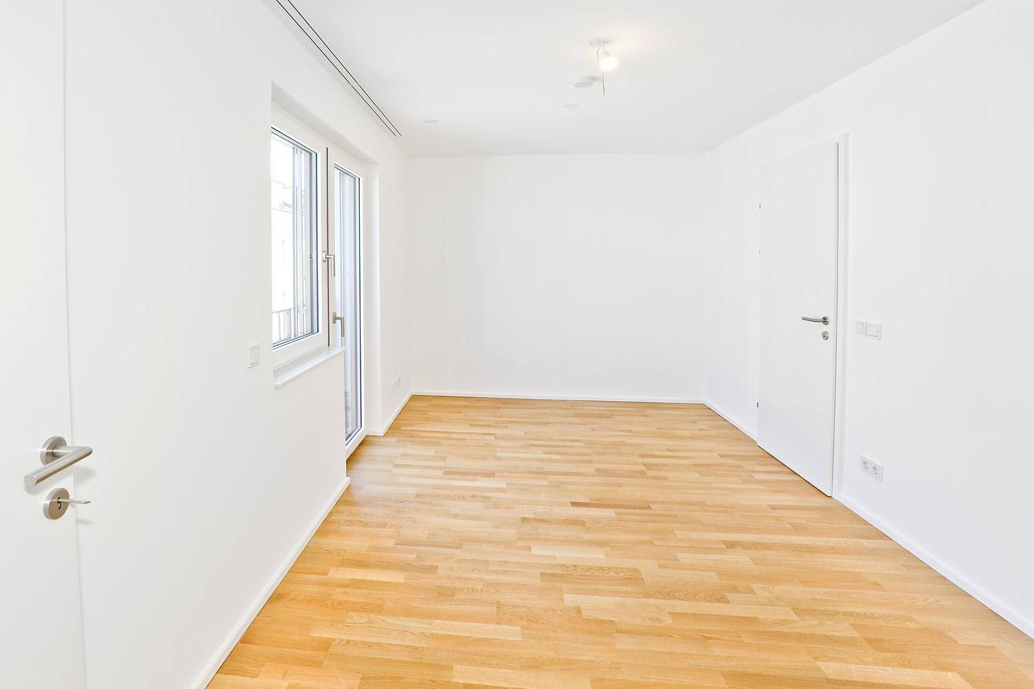 Helles Schlafzimmer mit Parkettboden und großem Fenster.