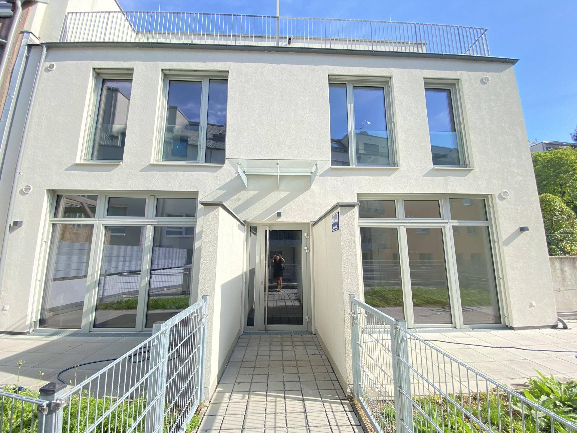 Eingangsbereich eines modernen Gebäudes mit Rampe und großen Fenstern unter blauem Himmel.