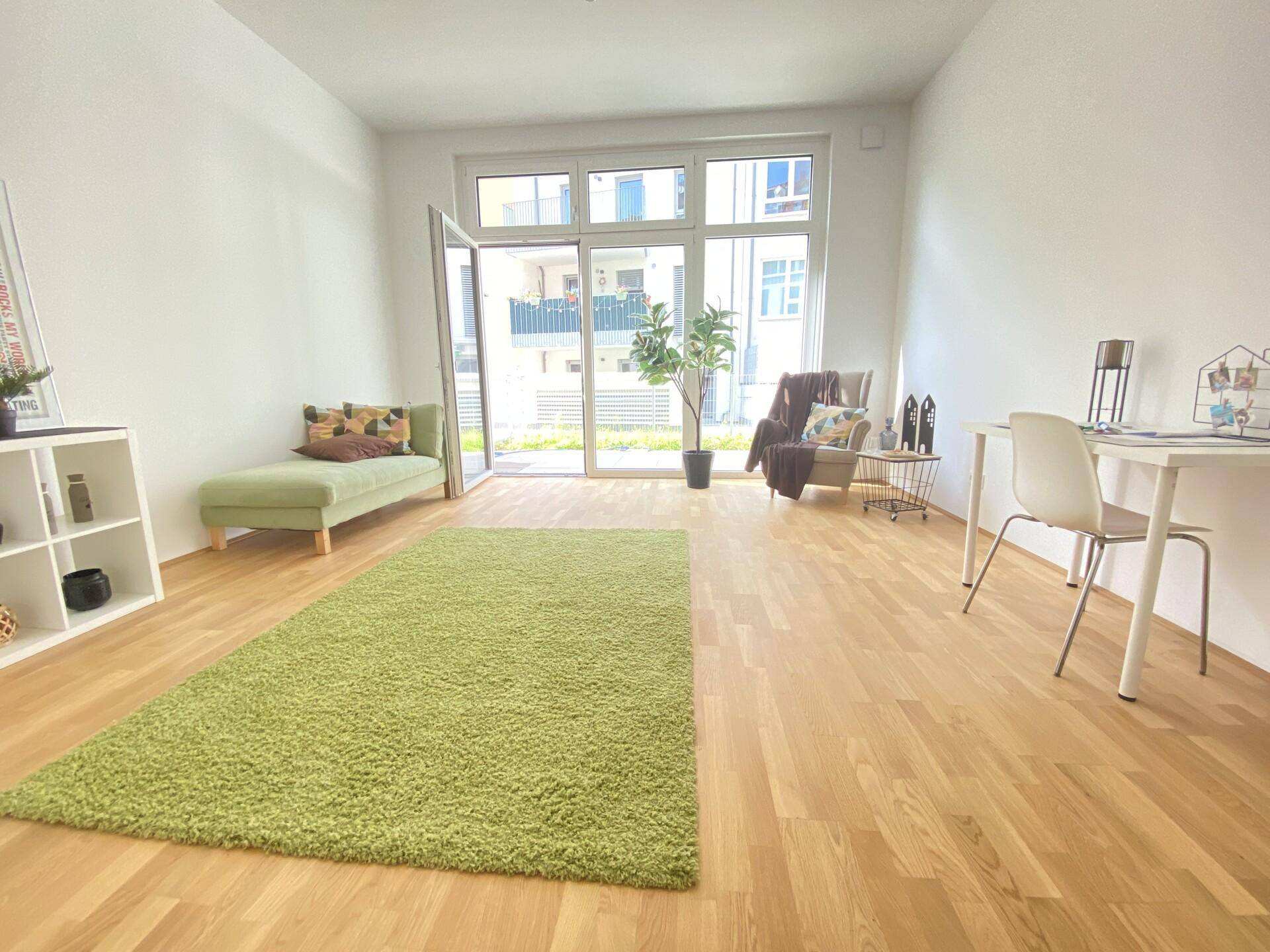 Geräumiges Wohnzimmer mit Holzboden, einem großen grünen Teppich und Zugang zu einer Terrasse.