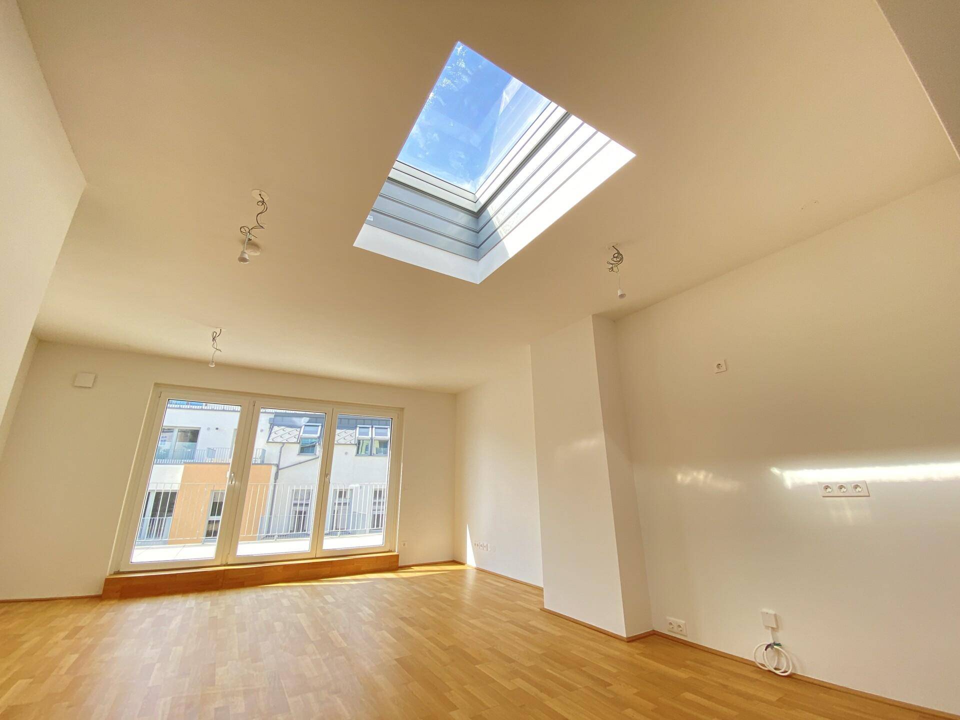 Heller Wohnraum mit Parkettboden, großen Fenstern und einem Dachfenster für viel Tageslicht.