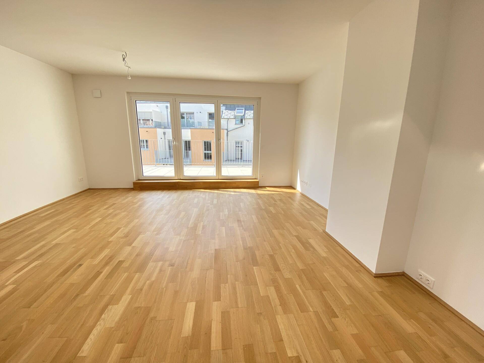 Heller Wohnraum mit Parkettboden und großen Fenstern, die viel Tageslicht hereinlassen.