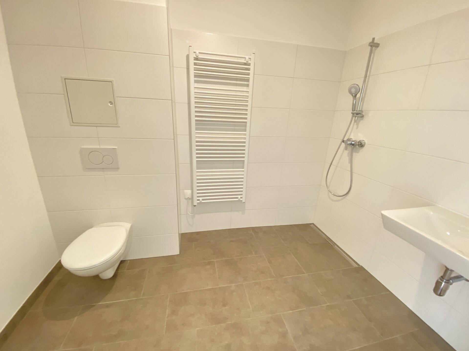Modernes Badezimmer mit weißen Fliesen, ebenerdiger Dusche, Wand-WC und Handtuchheizkörper.
