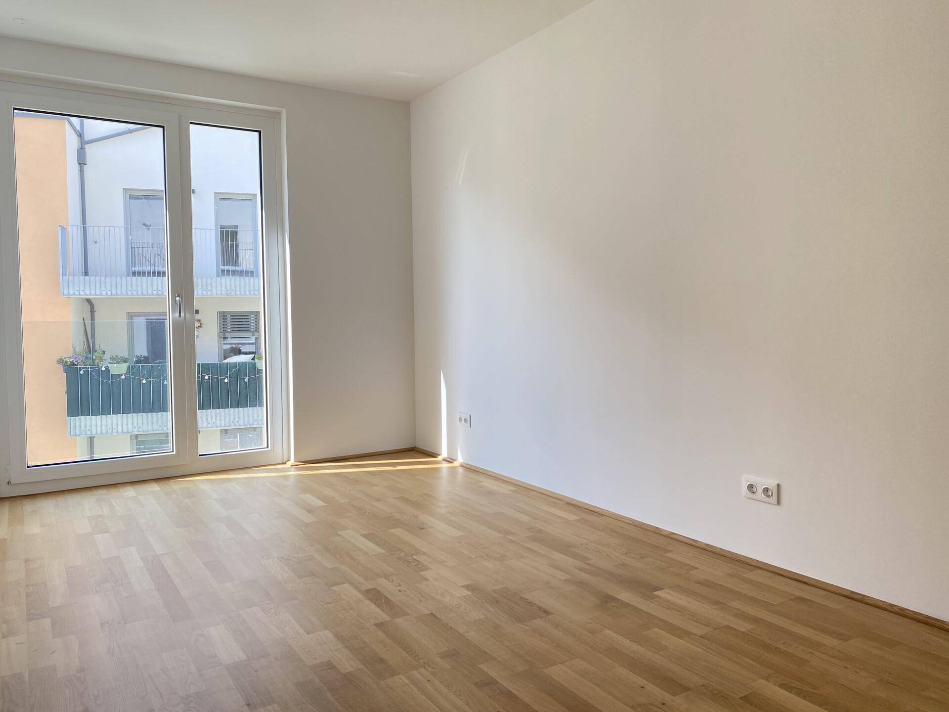 Helles Zimmer mit Parkettboden und Zugang zu einem Balkon oder einer Terrasse.
