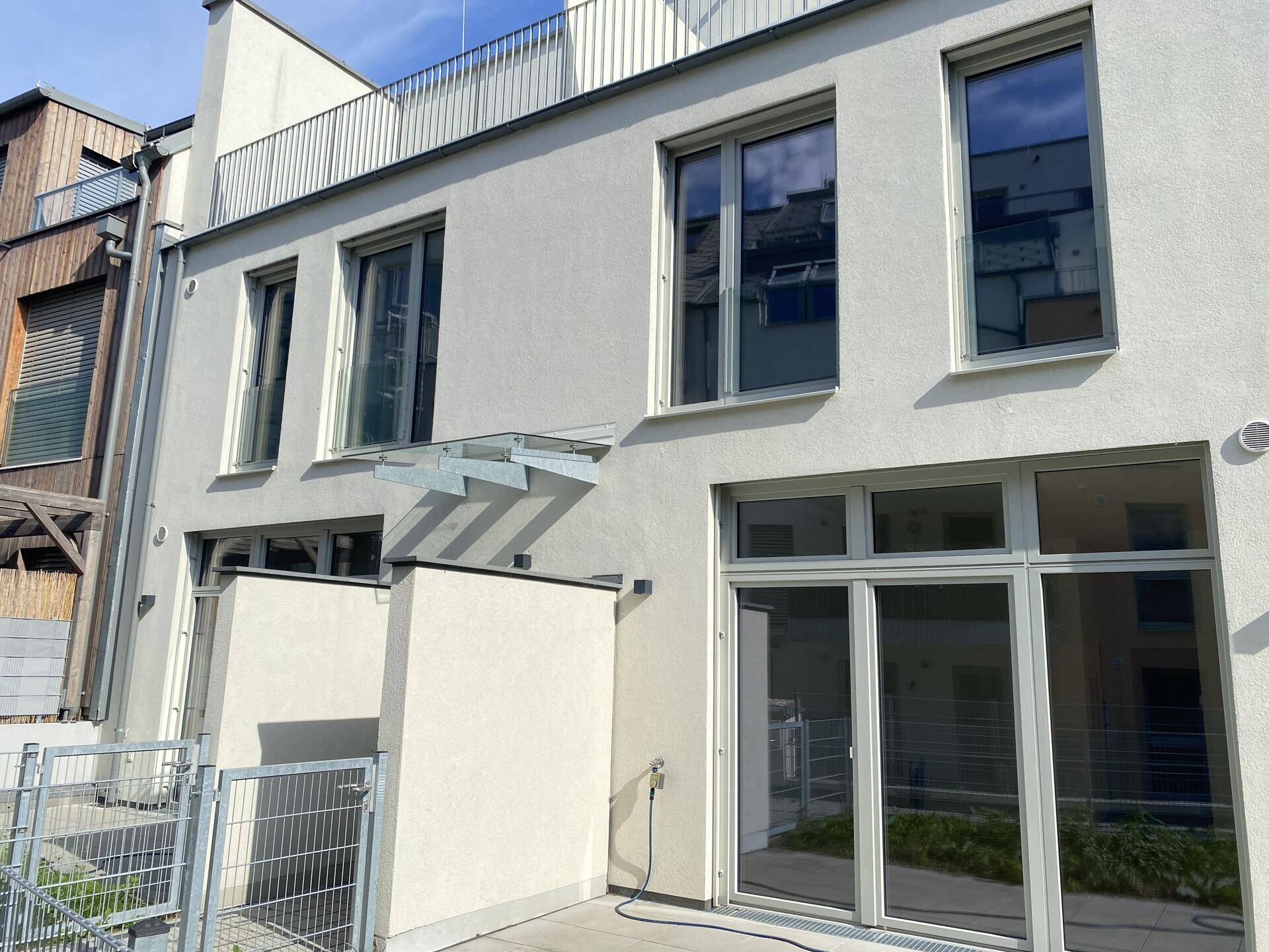 Seitenansicht des modernen Gebäudes mit einer kleinen gepflasterten Terrasse im Erdgeschoss.