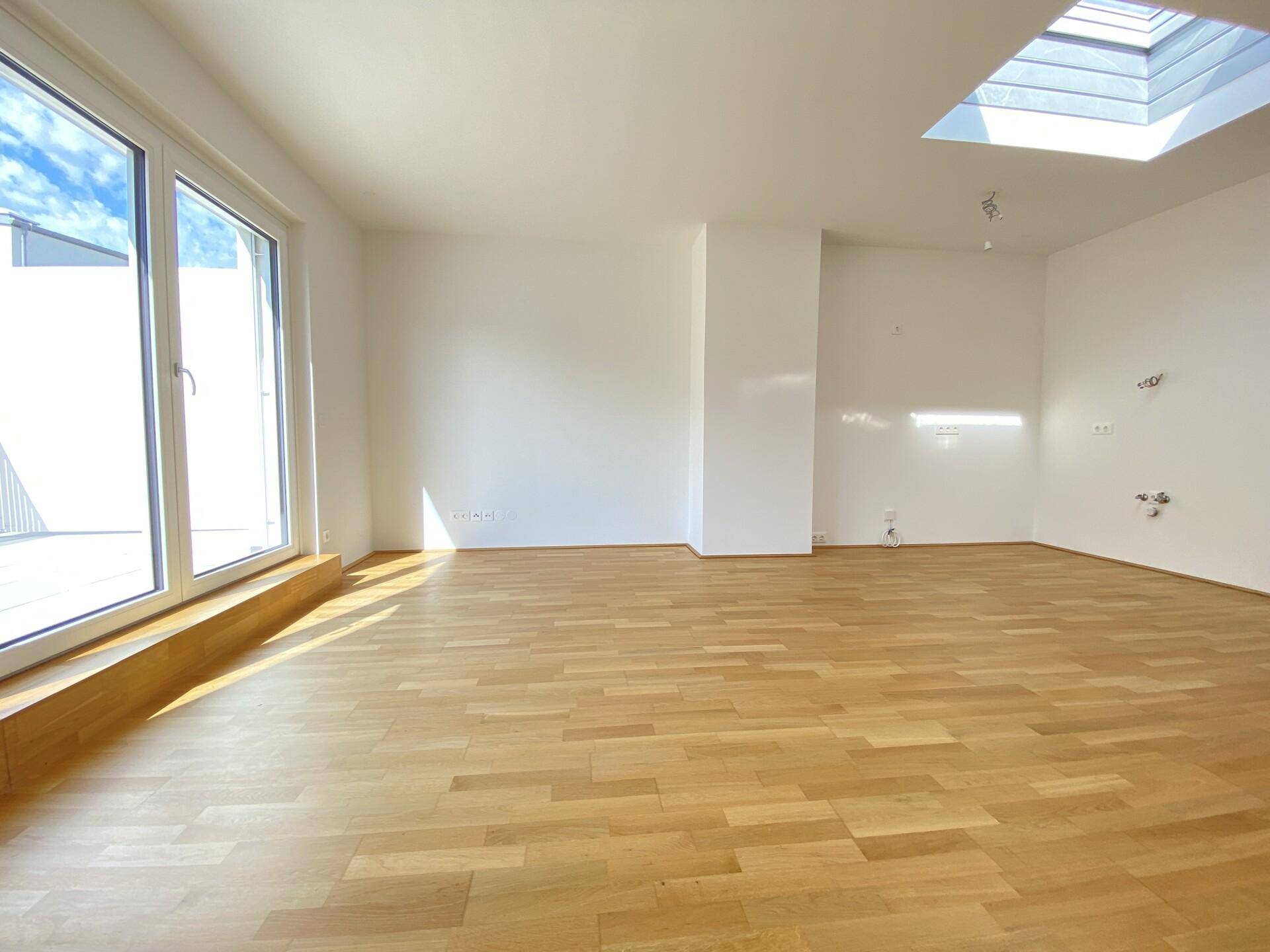 Geräumiger Wohnbereich mit Parkettboden, Dachfenster und Zugang zu einem sonnigen Außenbereich.