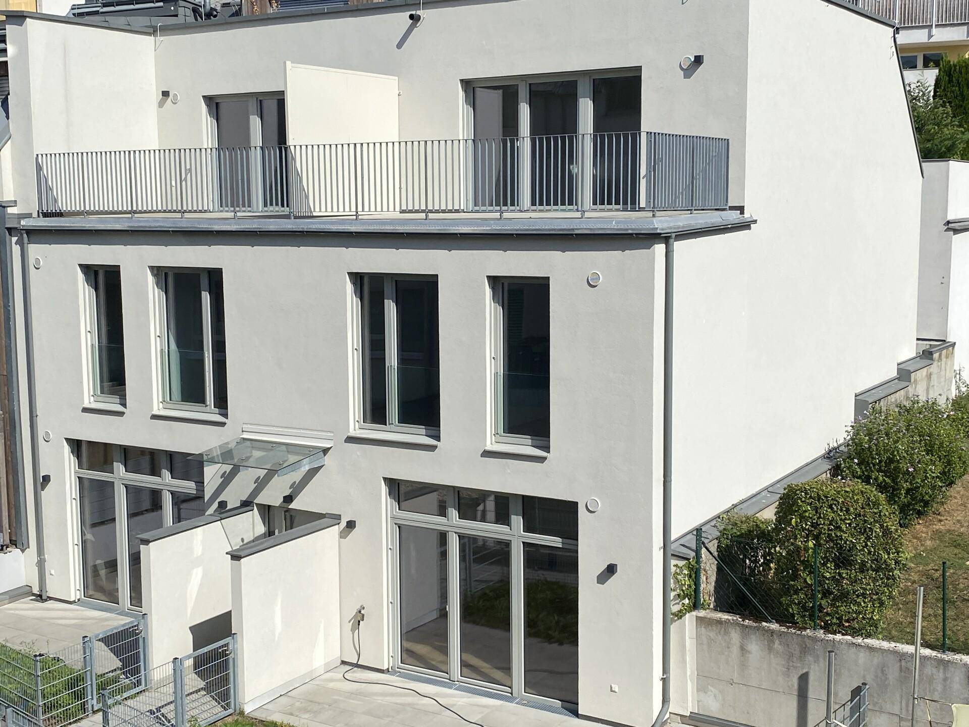 Seitenansicht des Neubaus mit Balkon, Terrasse und einem kleinen Gartenbereich.