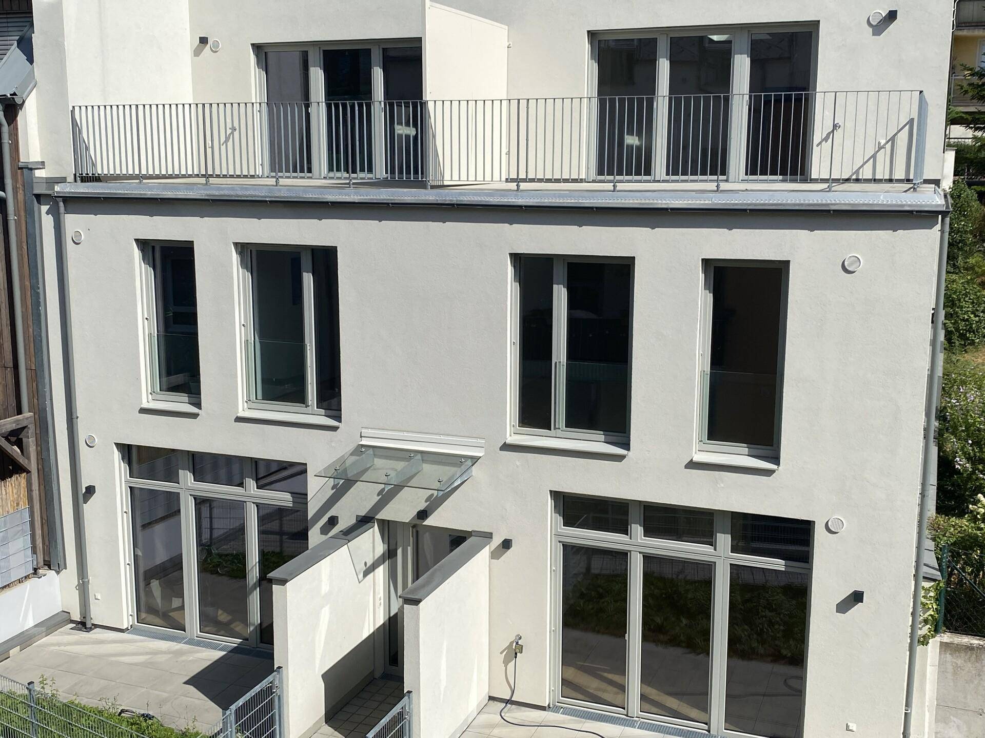 Ansicht der modernen Gebäudefassade von oben mit Balkon im Obergeschoss und Eingangsbereich.