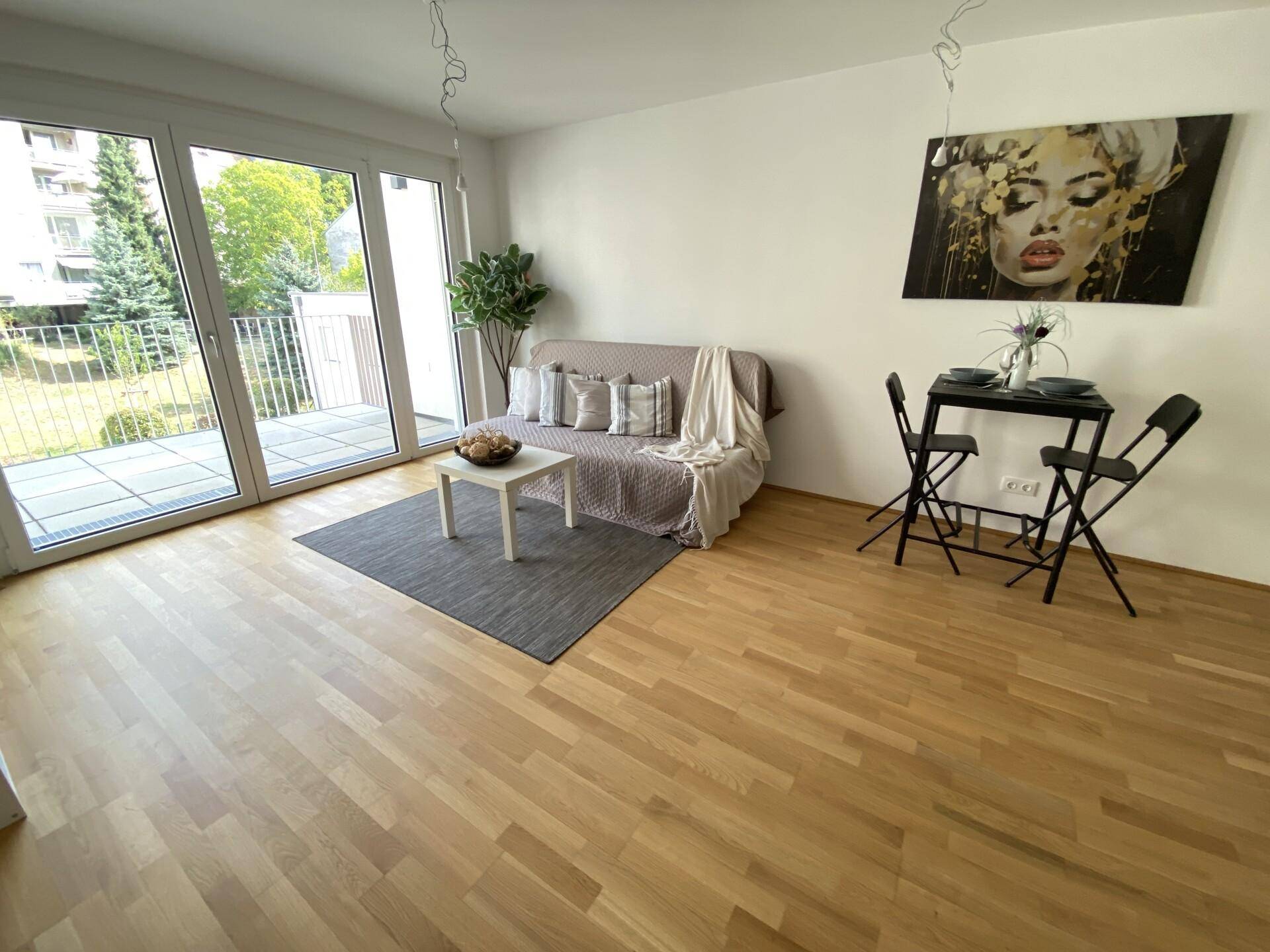 Lichtdurchfluteter Wohnbereich mit Holzboden, Sofa und Essgelegenheit, mit Blick ins Grüne.