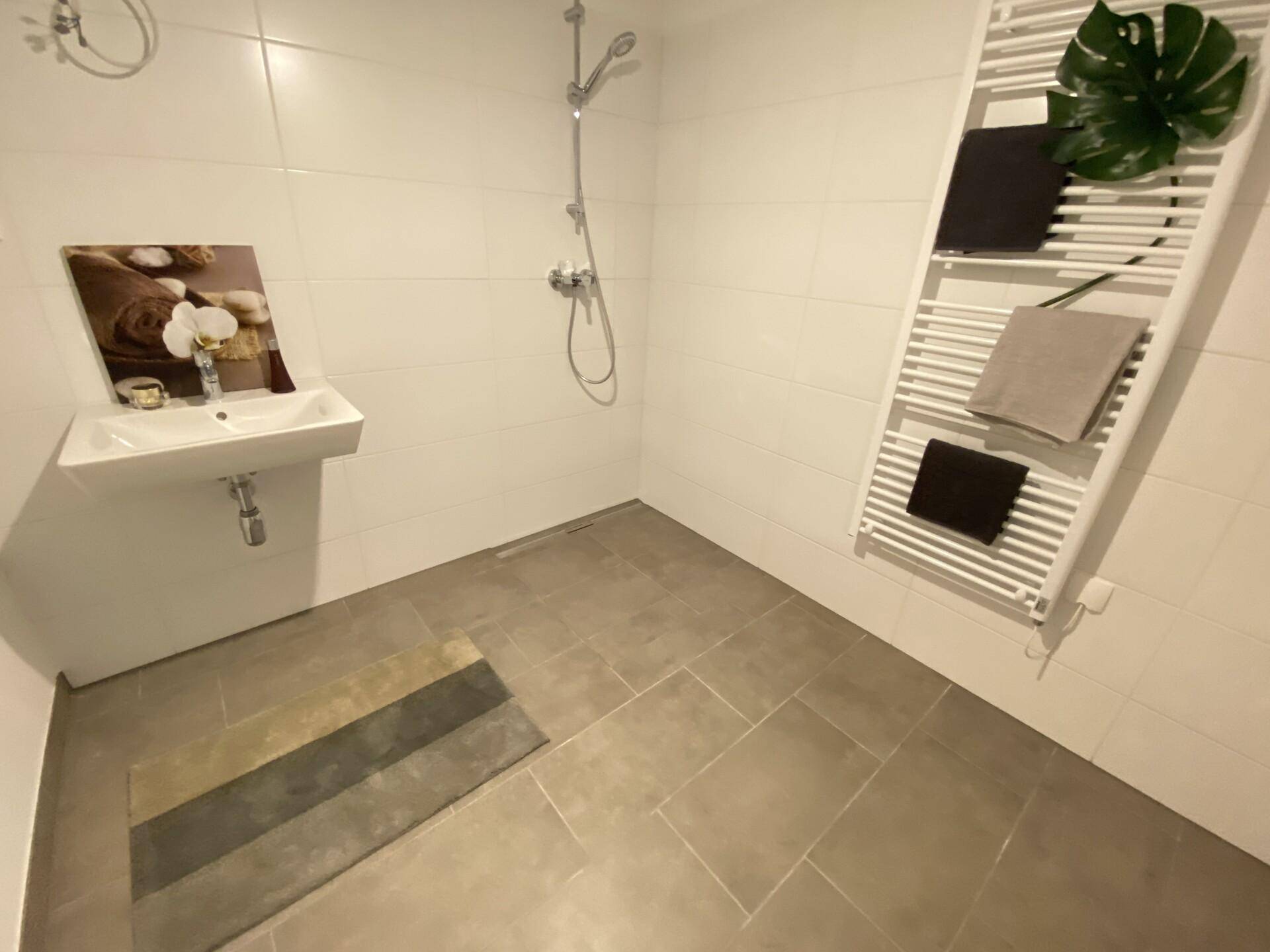 Modernes Badezimmer mit ebenerdiger Dusche, Wandwaschbecken und Handtuchheizkörper.