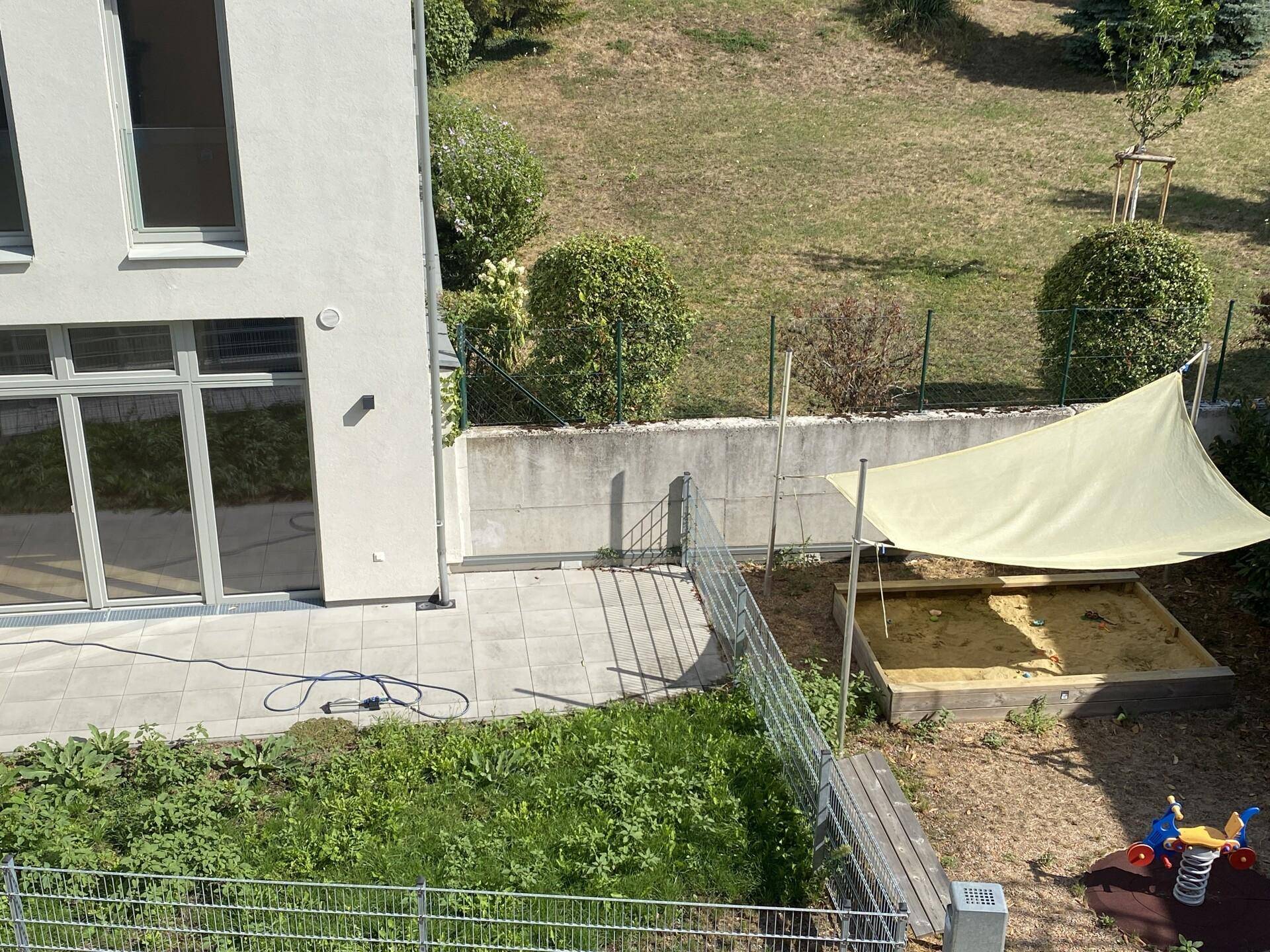 Außenbereich mit Terrasse, kleinem Garten und einem Sandkasten mit Sonnenschutz.
