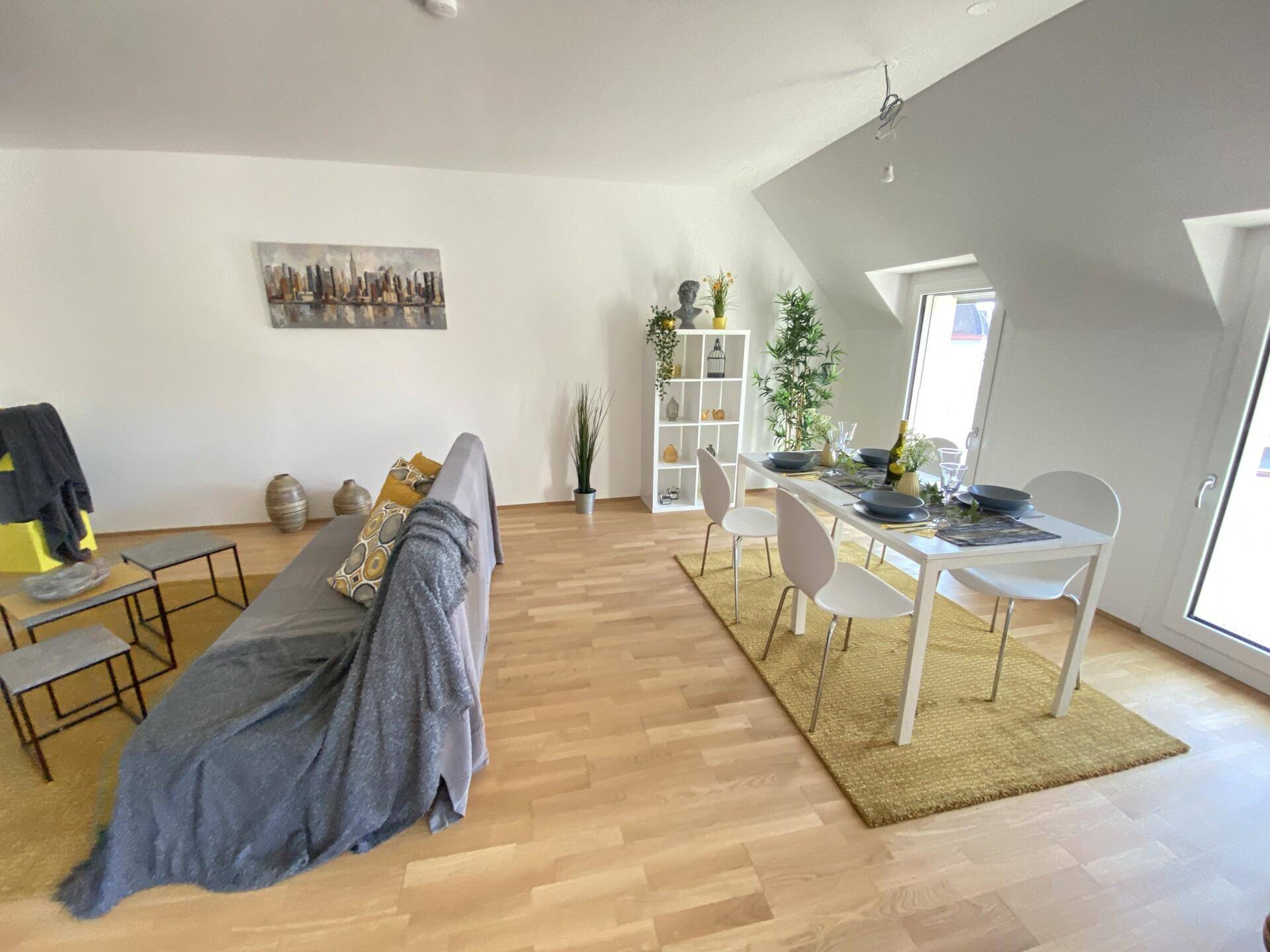 Offener Wohn- und Essbereich mit Holzboden, gemütlichem Sofa und schrägen Decken.