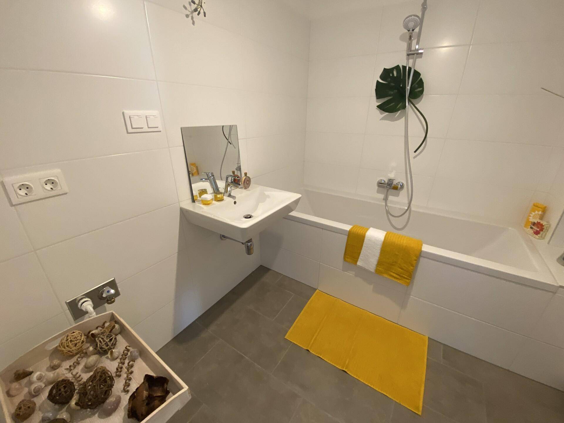 Modernes Badezimmer mit weißen Fliesen, Badewanne mit Duschfunktion und Einzelwaschbecken.
