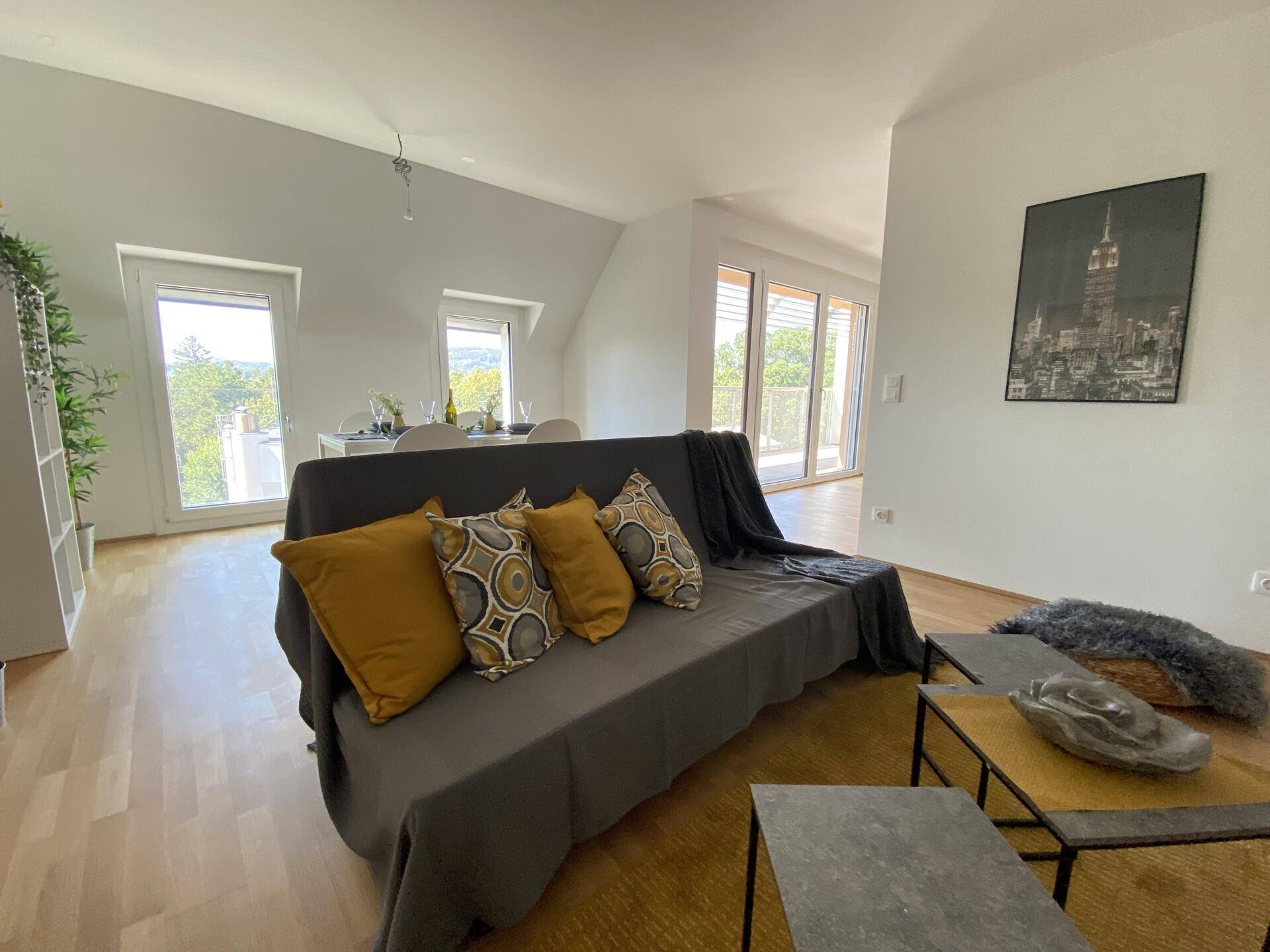 Wohnzimmer mit bequemem Sofa, Holzboden und Blick auf den Essbereich und die Terrasse.