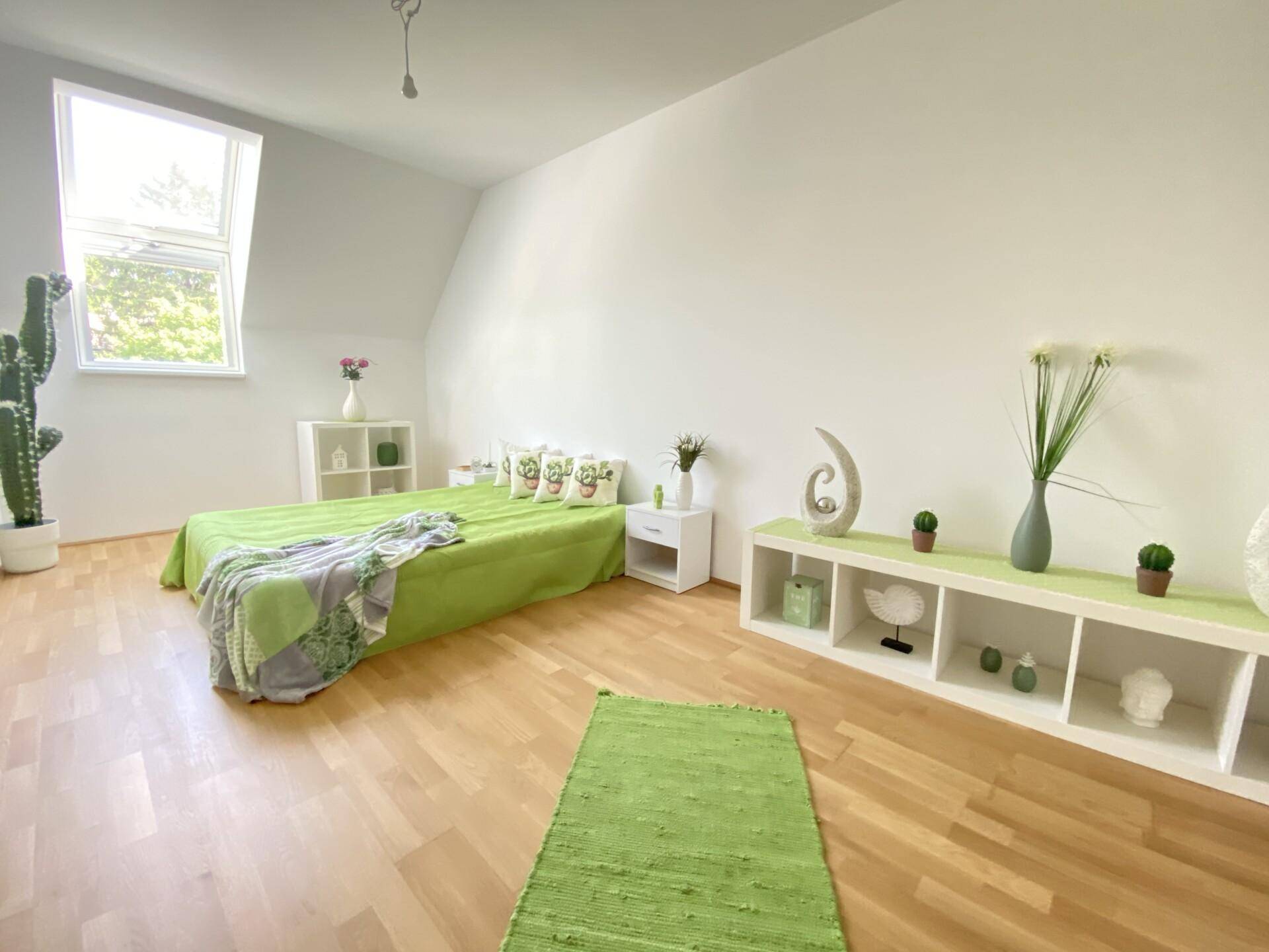 Helles Schlafzimmer mit Holzboden, grüner Dekoration und einem Dachfenster für viel Licht.
