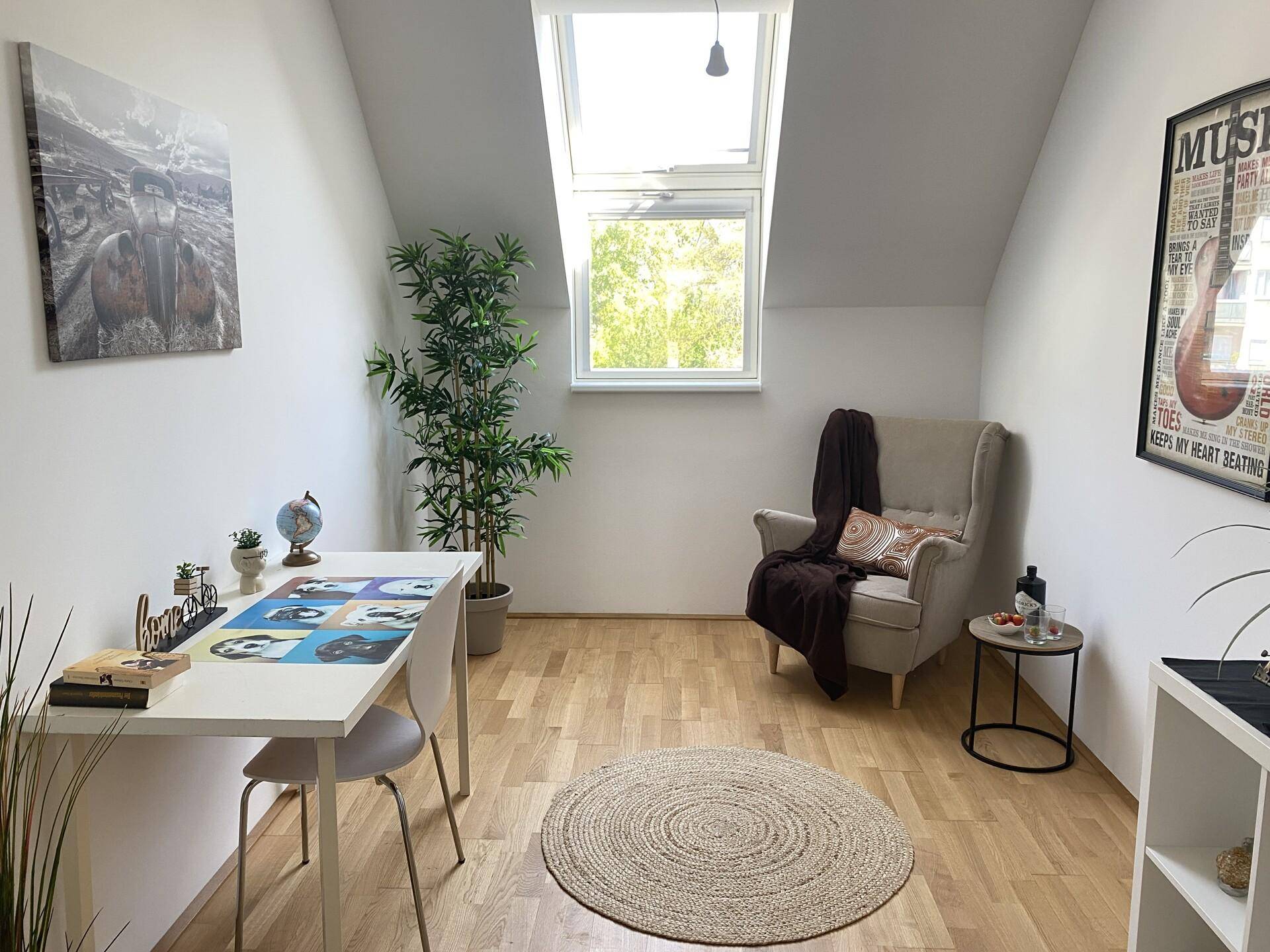 Ruhiges Arbeitszimmer mit Holzboden, Schreibtisch und gemütlichem Sessel unter einem Dachfenster.