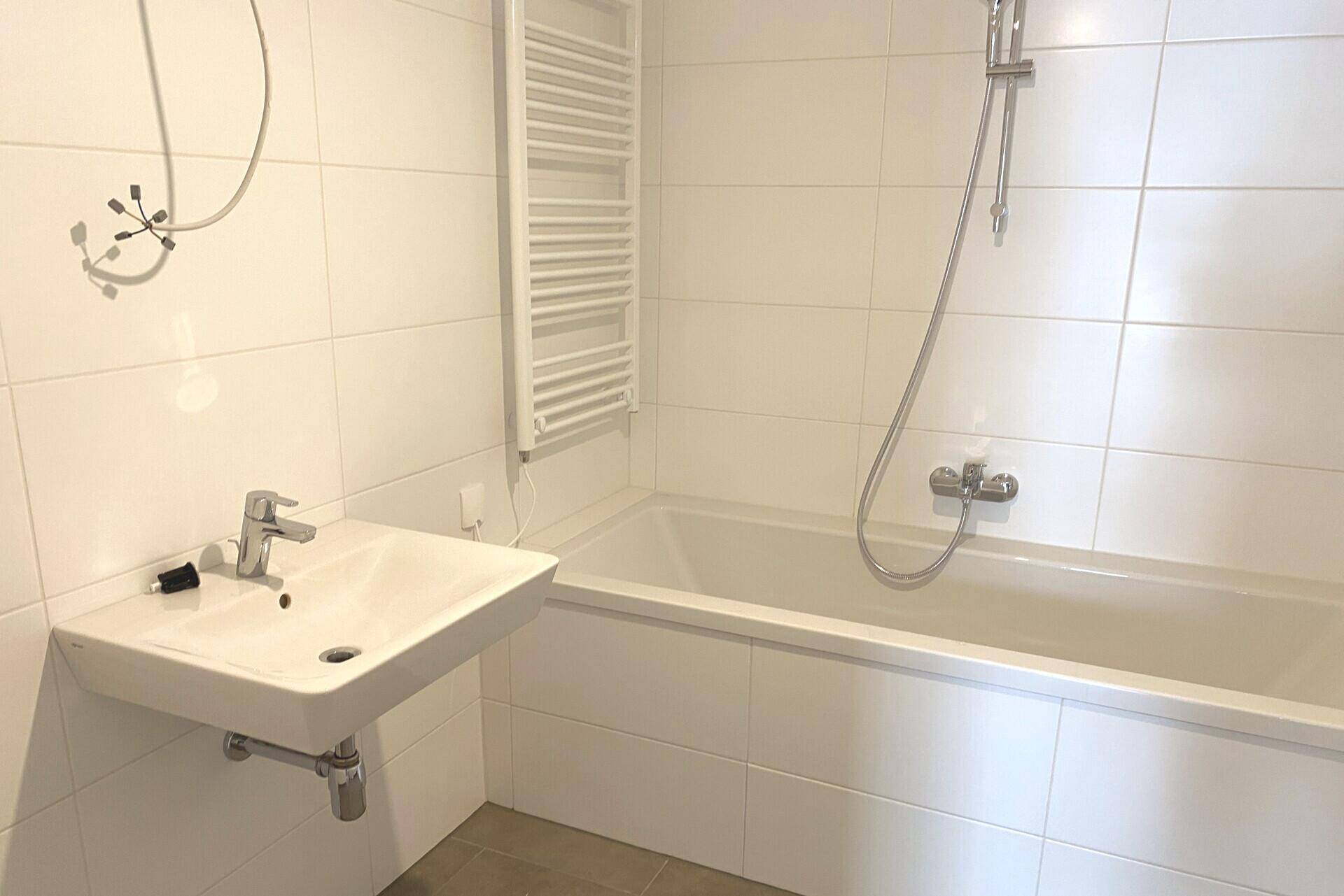 Modernes Badezimmer mit weißen Fliesen, Badewanne mit Duschfunktion und beheiztem Handtuchhalter.