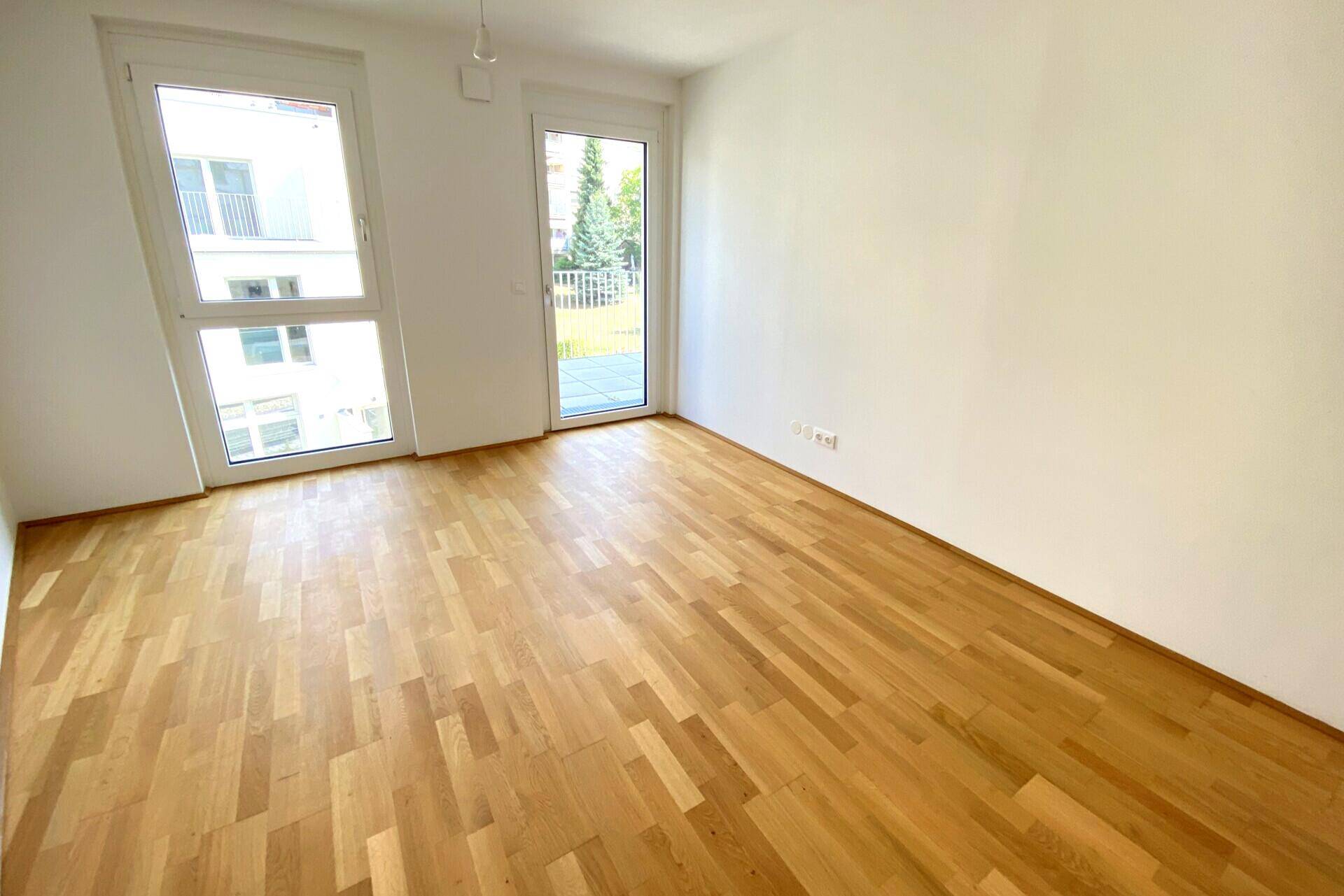 Geräumiges Schlafzimmer mit hellem Parkett und Fensterfront, die viel Tageslicht spendet.