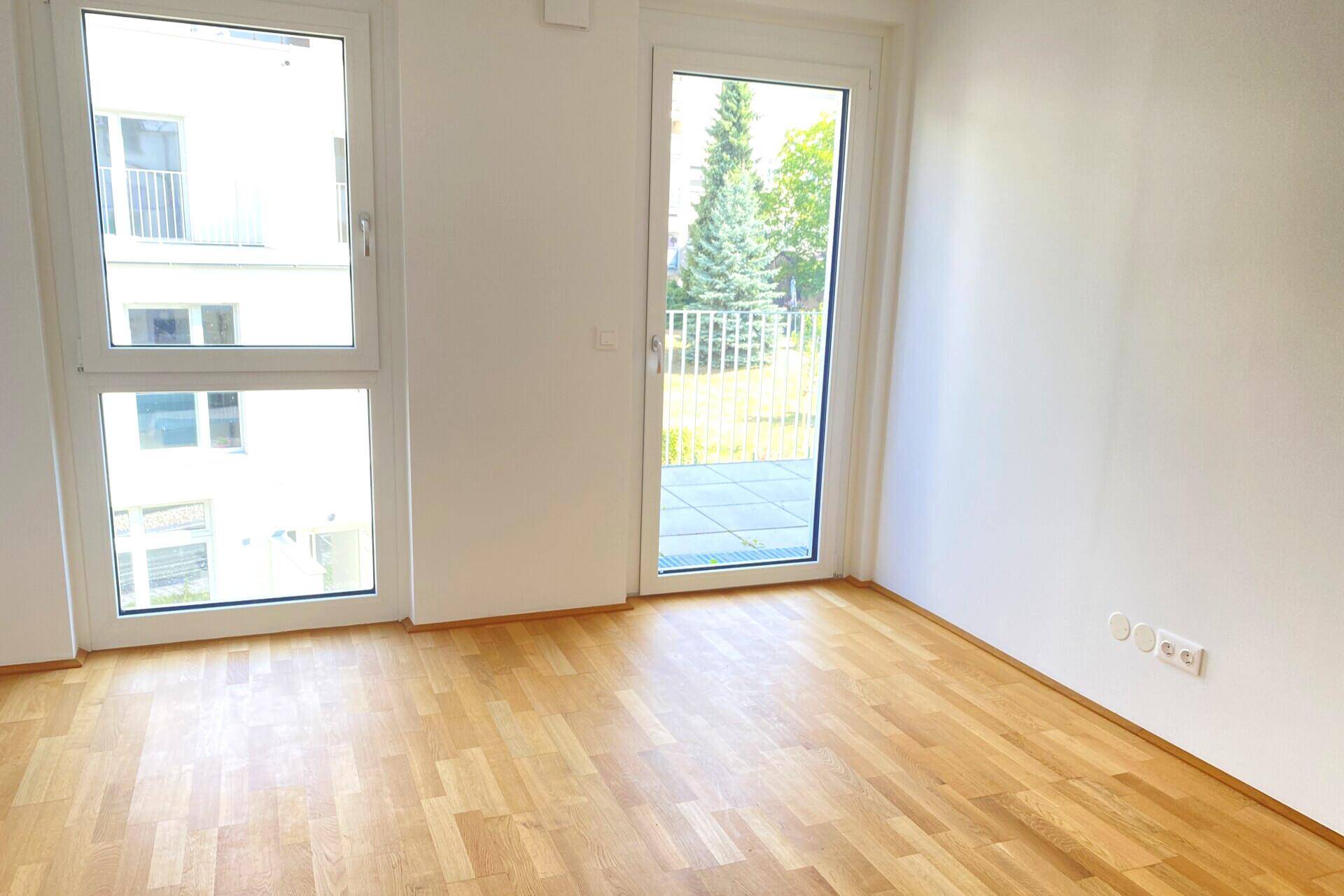 Helles Schlafzimmer mit Parkettboden und direktem Zugang zu einem kleinen Balkon.
