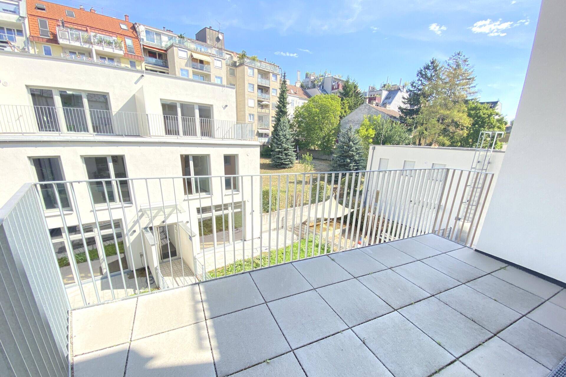 Geräumiger Balkon mit Fliesenboden und Blick auf den grünen Innenhof und umliegende Gebäude.