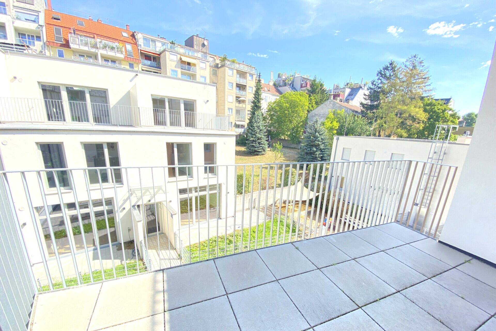 Weitläufiger Balkon mit Fliesen und Blick auf den begrünten Innenhof und die umliegende Bebauung.