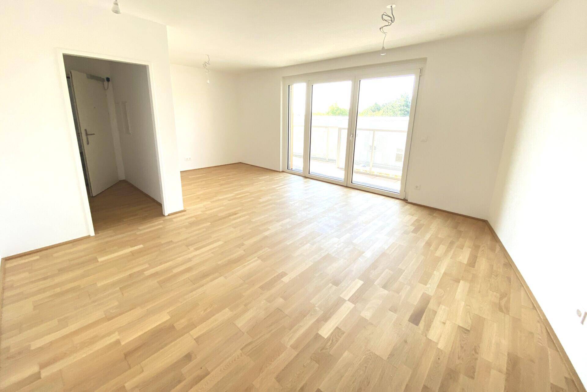 Heller Wohnraum mit Parkettboden und Zugang zu einem Balkon, ideal für individuelle Gestaltung.
