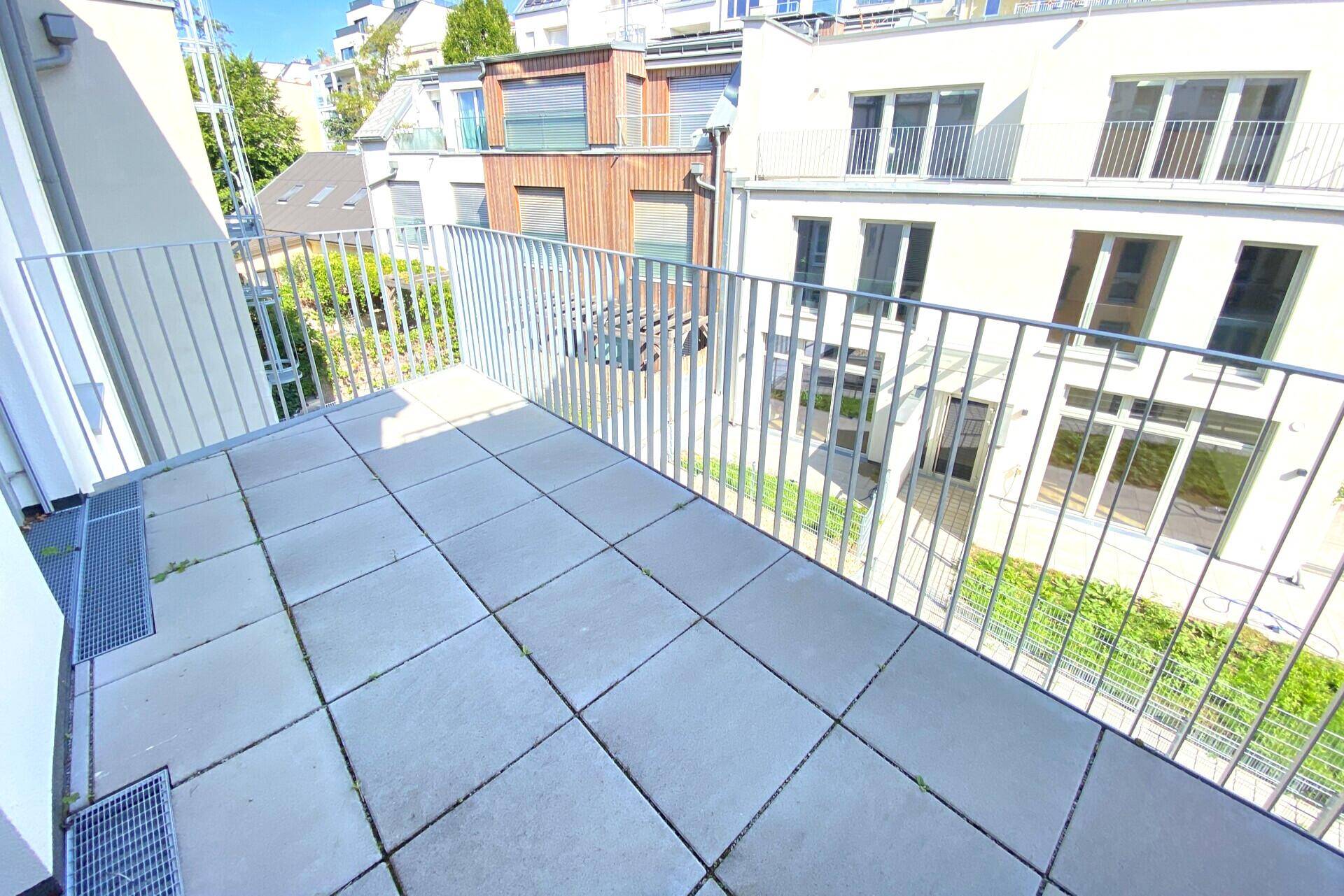 Heller Balkon mit Fliesenboden und Aussicht auf den ruhigen Innenhof und die Nachbargebäude.