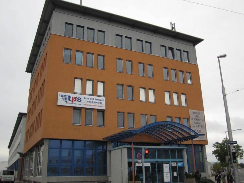 Modernes Bürogebäude mit orangefarbener Fassade, blauen Akzenten und vielen Fenstern.