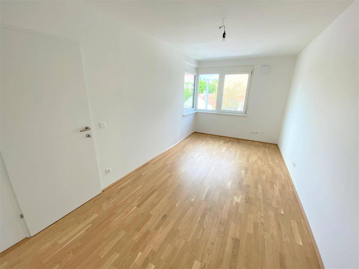 Helles Schlafzimmer mit Parkettboden und Fenster, bereit zur individuellen Gestaltung.