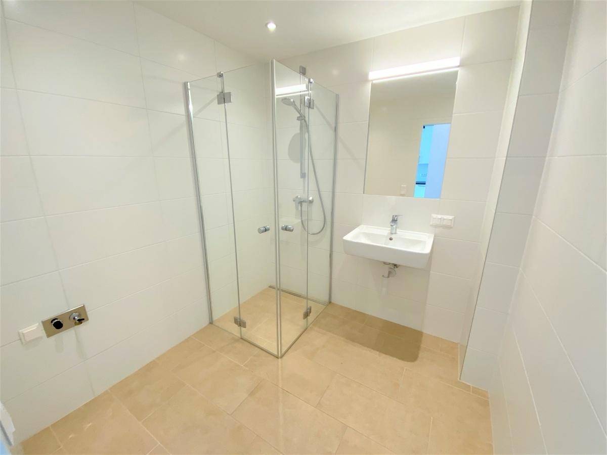 Modernes Badezimmer mit Duschkabine aus Glas und weiß gefliesten Wänden.