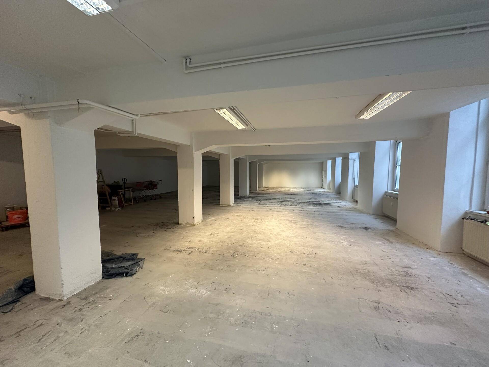 Geräumiger, leerer Gewerberaum mit Betonboden, Säulen und Fenstern, geeignet für verschiedene Geschäftszwecke.