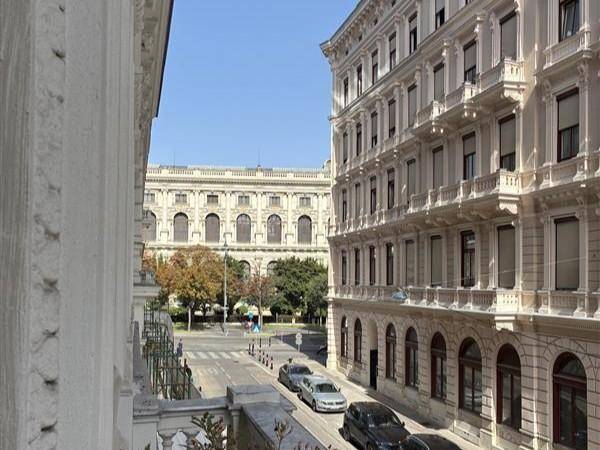 Blick von einem Fenster auf eine belebte Straße mit historischen Gebäuden, parkenden Autos und Bäumen.