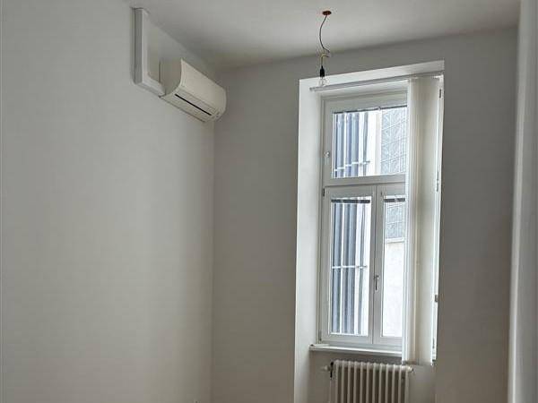 Helles Schlafzimmer mit Klimaanlage, einem Fenster mit Jalousien und einem Heizkörper, bereit zur Nutzung.