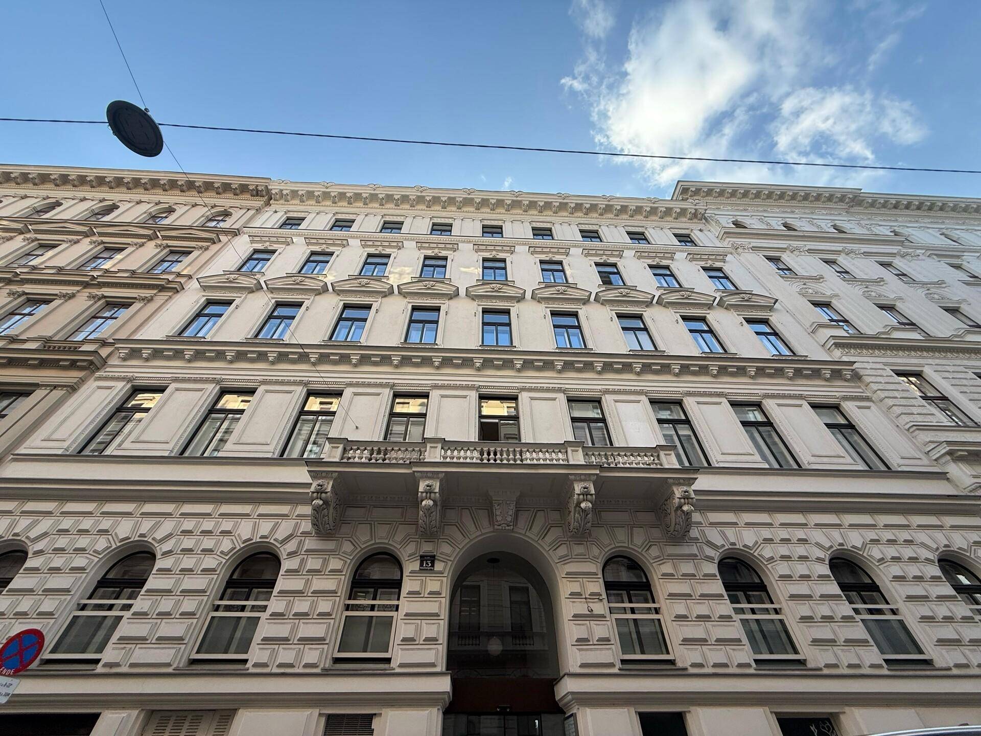 Prächtige Fassade eines Altbaus mit reich verzierten Details und einem zentralen Balkon unter blauem Himmel.