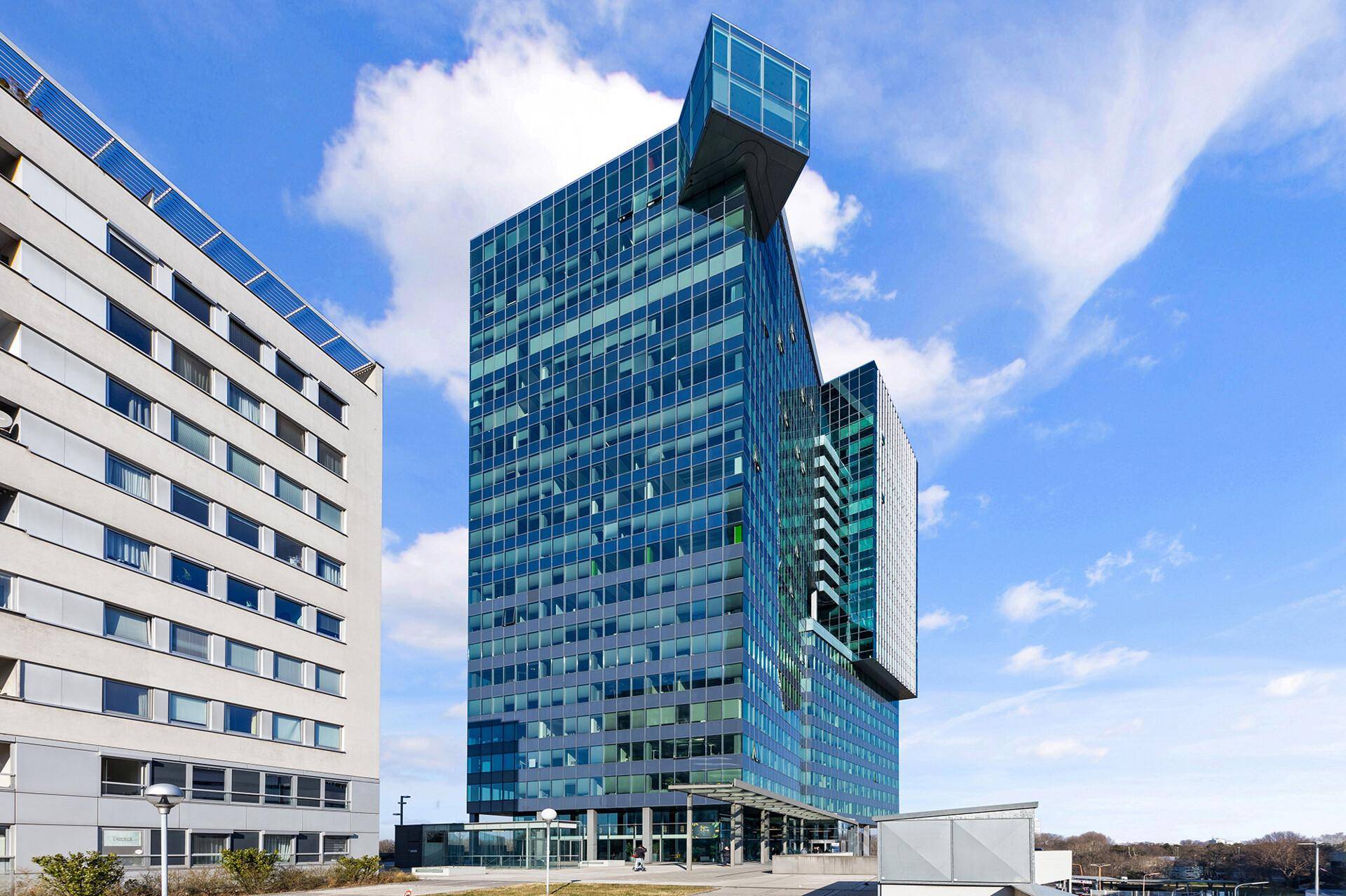 Modernes Hochhaus mit Glasfassade und einzigartiger Architektur unter blauem Himmel.