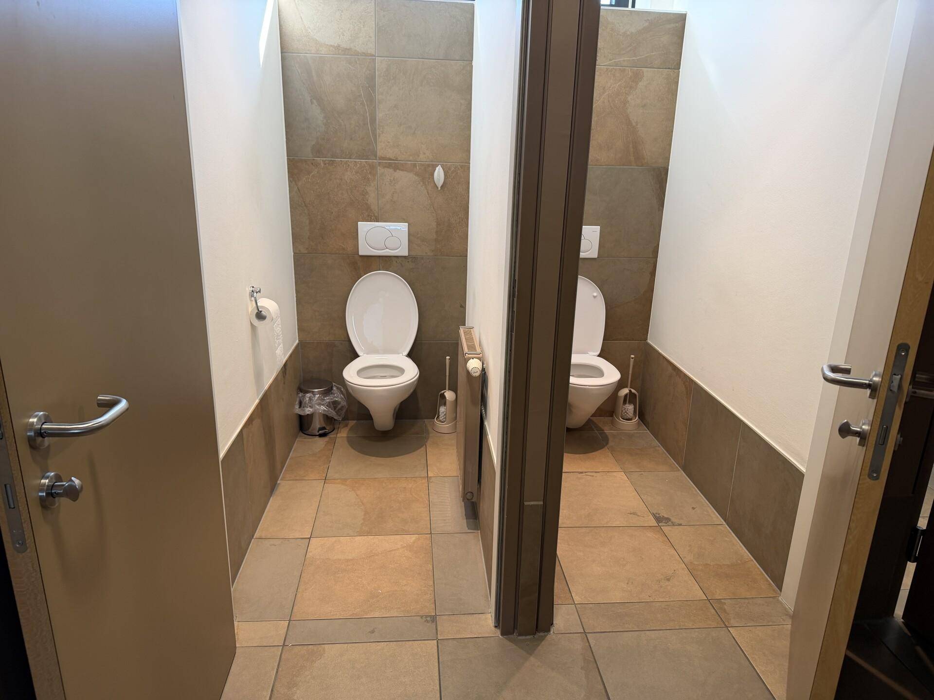 Zwei separate Toilettenkabinen mit modernen Wand- und Bodenfliesen in einem Waschraum.