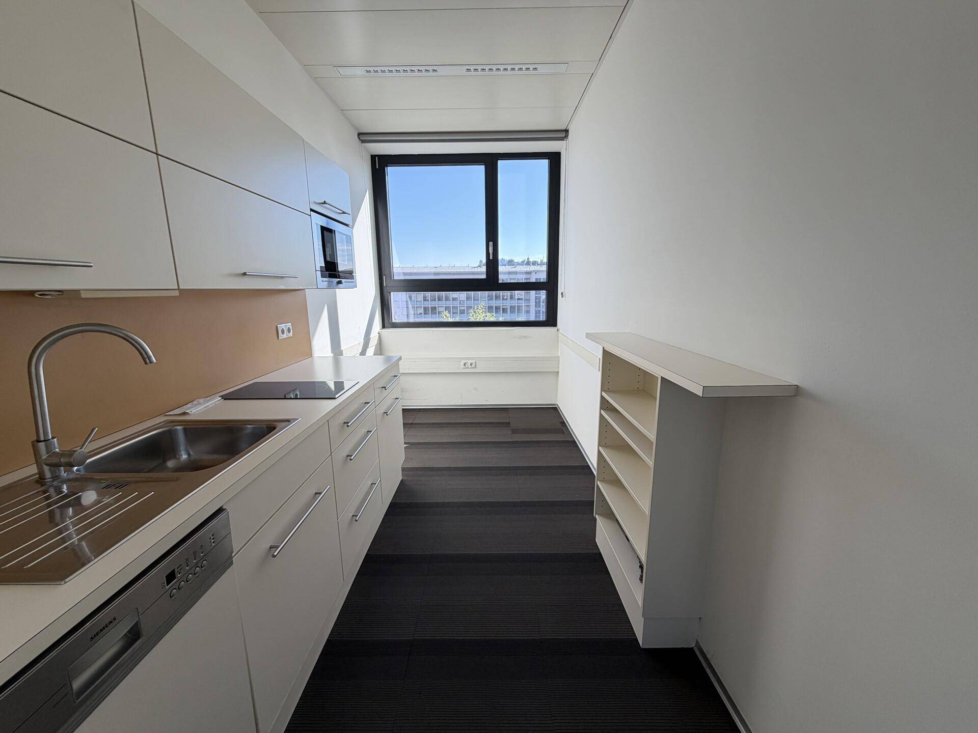 Moderne Küchenzeile mit weißen Schränken, Spüle und Einbaugeräten in einem Bürogebäude.