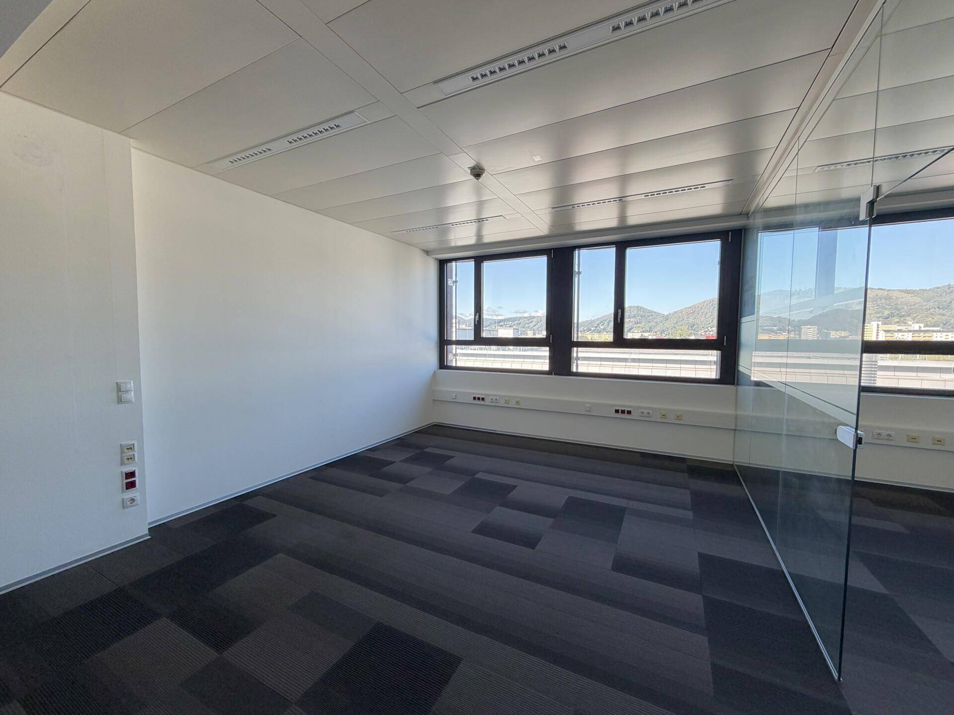 Helles Büro mit Teppichfliesen, Glasabtrennung und weitem Blick auf die Umgebung.