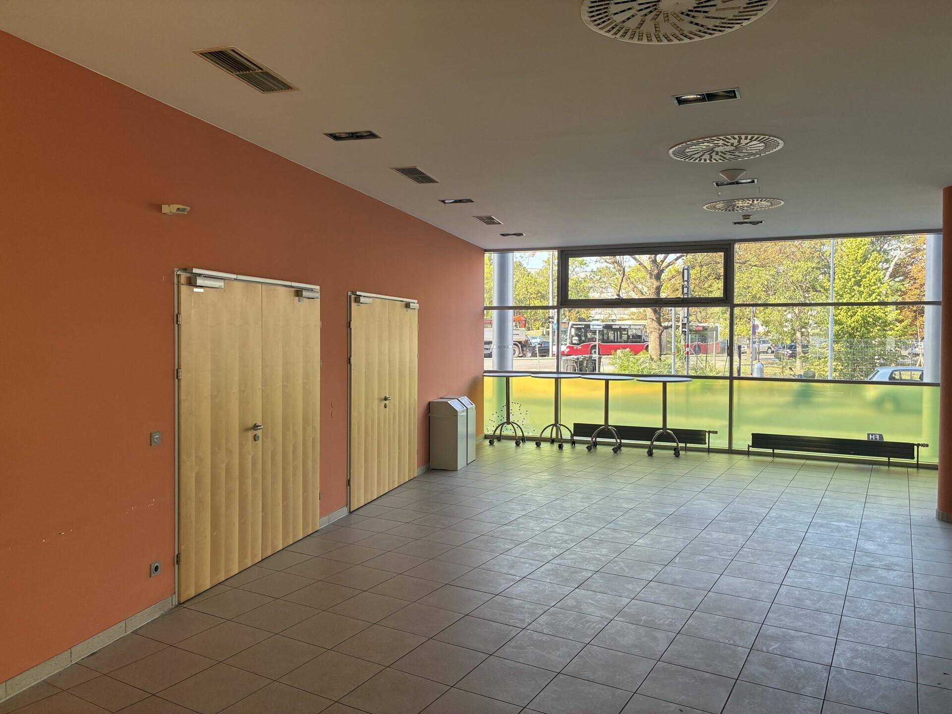 Geräumiger Flur mit großen Fenstern, orangefarbener Wand und Blick auf die Straße, ideal für Wartebereiche.