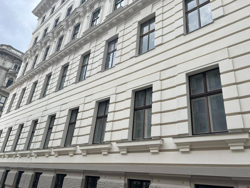 Klassische weiße Fassade eines Altbaus mit vielen Fenstern und dekorativen Gesimsen.