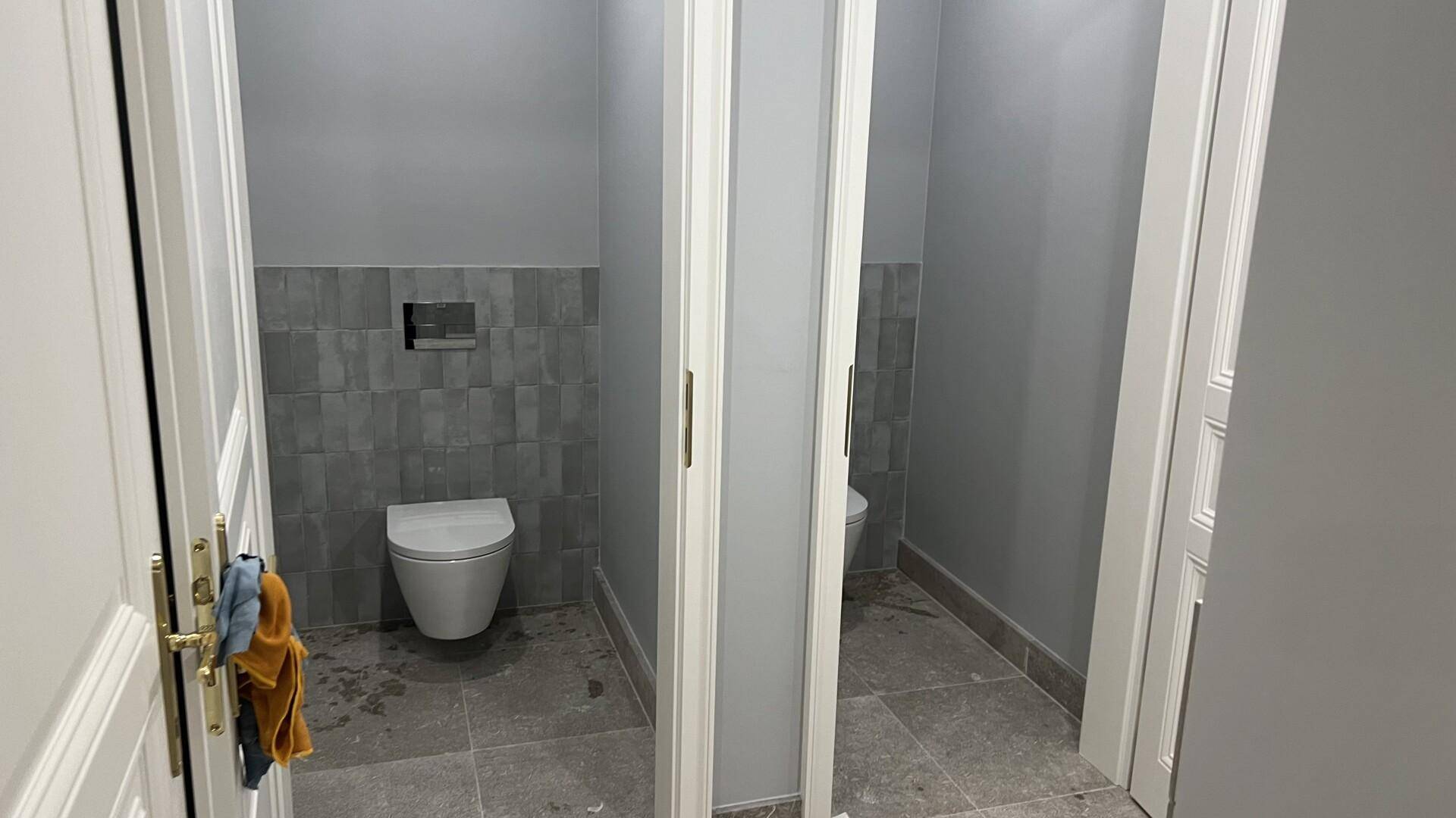 Zwei separate Toilettenkabinen mit modernen Wand-WCs und grauen Fliesen in einem Badezimmer.