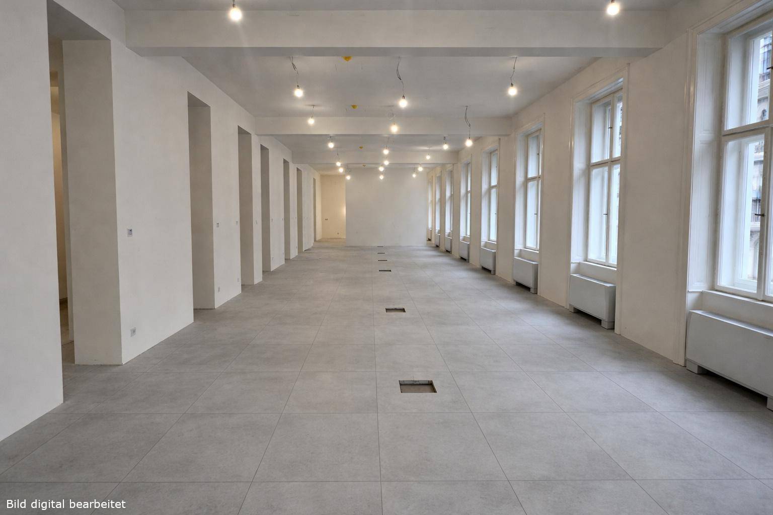 Großer, leerer Raum mit vielen Fenstern, hellem Fliesenboden und sichtbaren Deckenbalken, ideal für Büros.