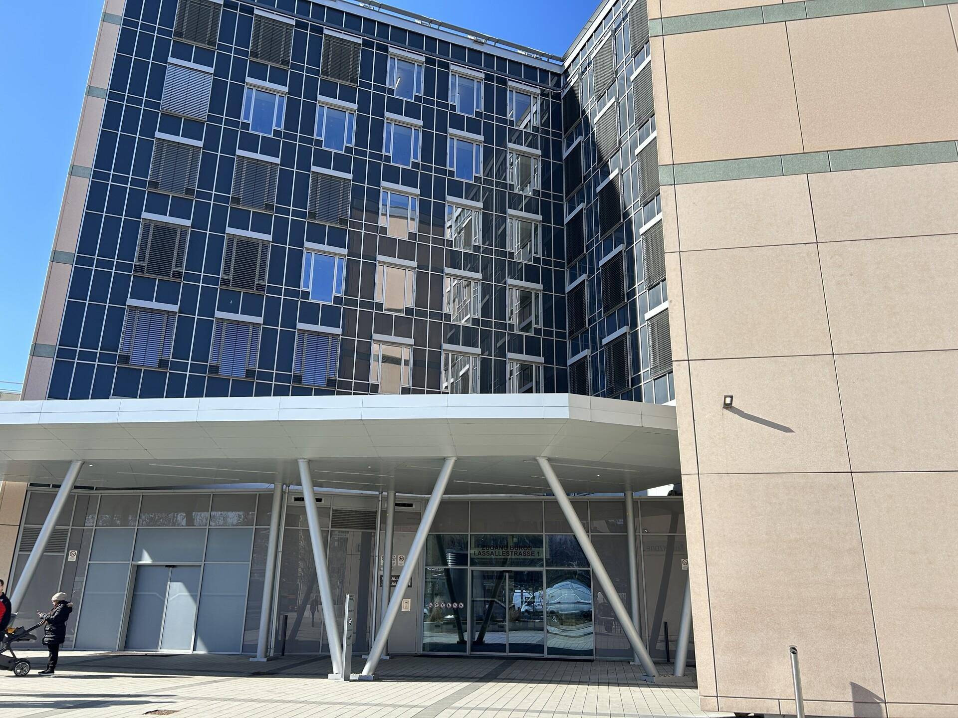 Eingangsbereich eines modernen Bürokomplexes mit großzügigem Vordach und Glasfassade.