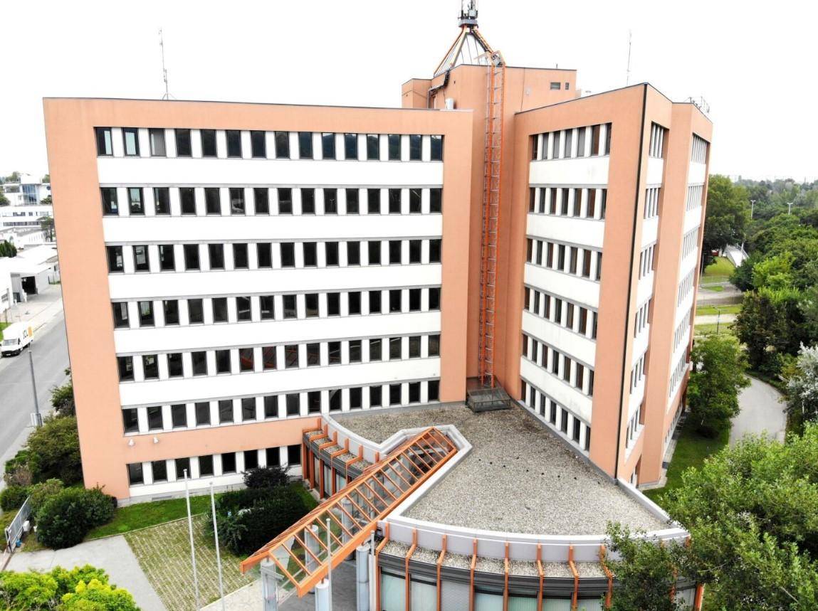 Luftaufnahme eines großen Bürogebäudes mit markanter Architektur, orangefarbener Fassade und vielen Fenstern.