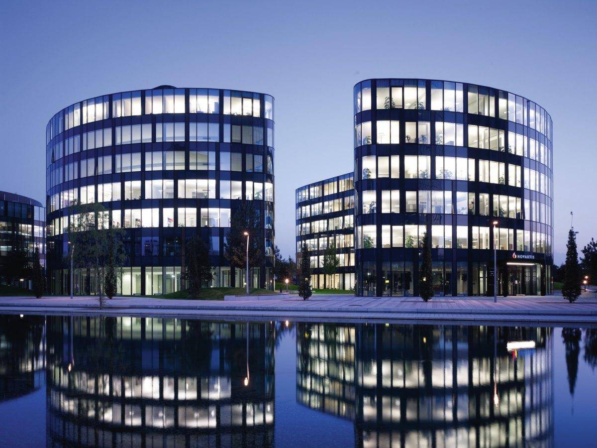 Moderne Bürogebäude mit beleuchteten Fenstern spiegeln sich nachts im ruhigen Wasser des Teiches.